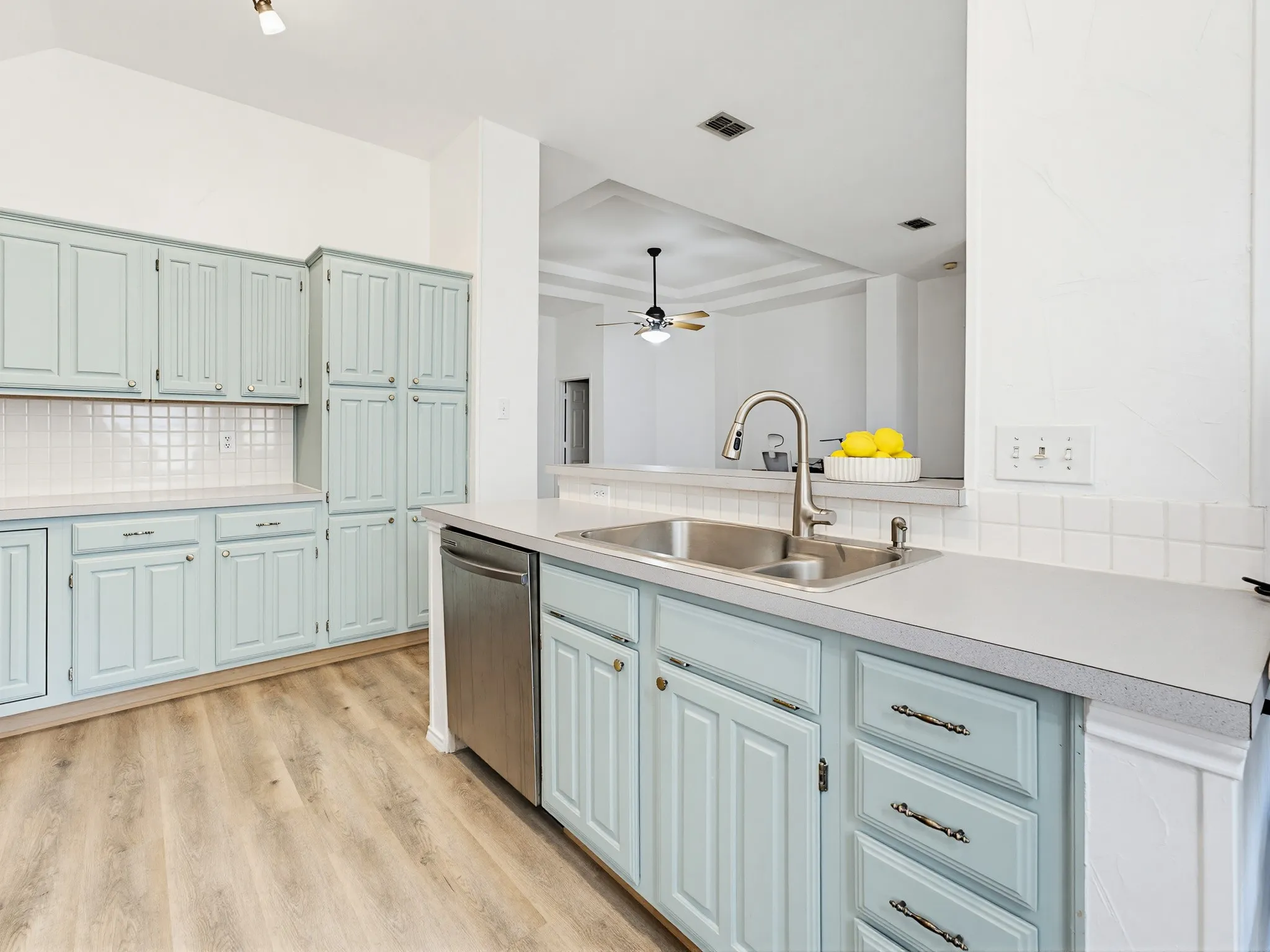 Kitchen featuring pale blue cabinetry, stainless steel sink, stainless steel dishwasher, white countertops, and wood-finish flooring