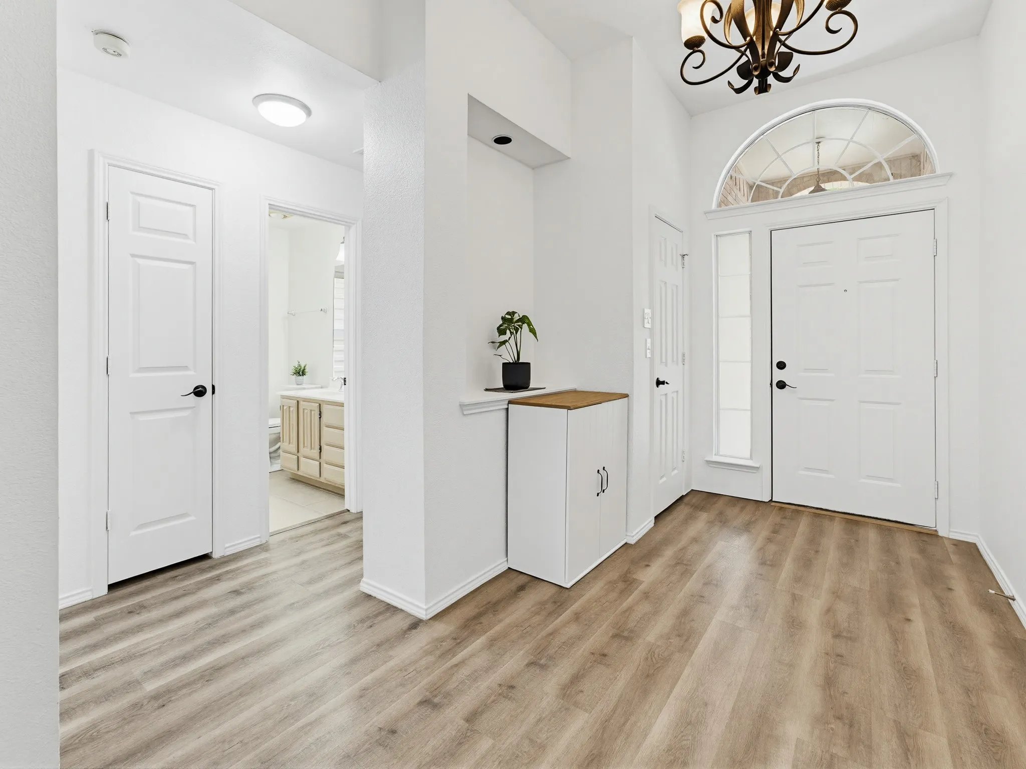 Entryway featuring wood-finish flooring, a white paneled door with sidelight and arched transom, a decorative chandelier, and recessed lighting