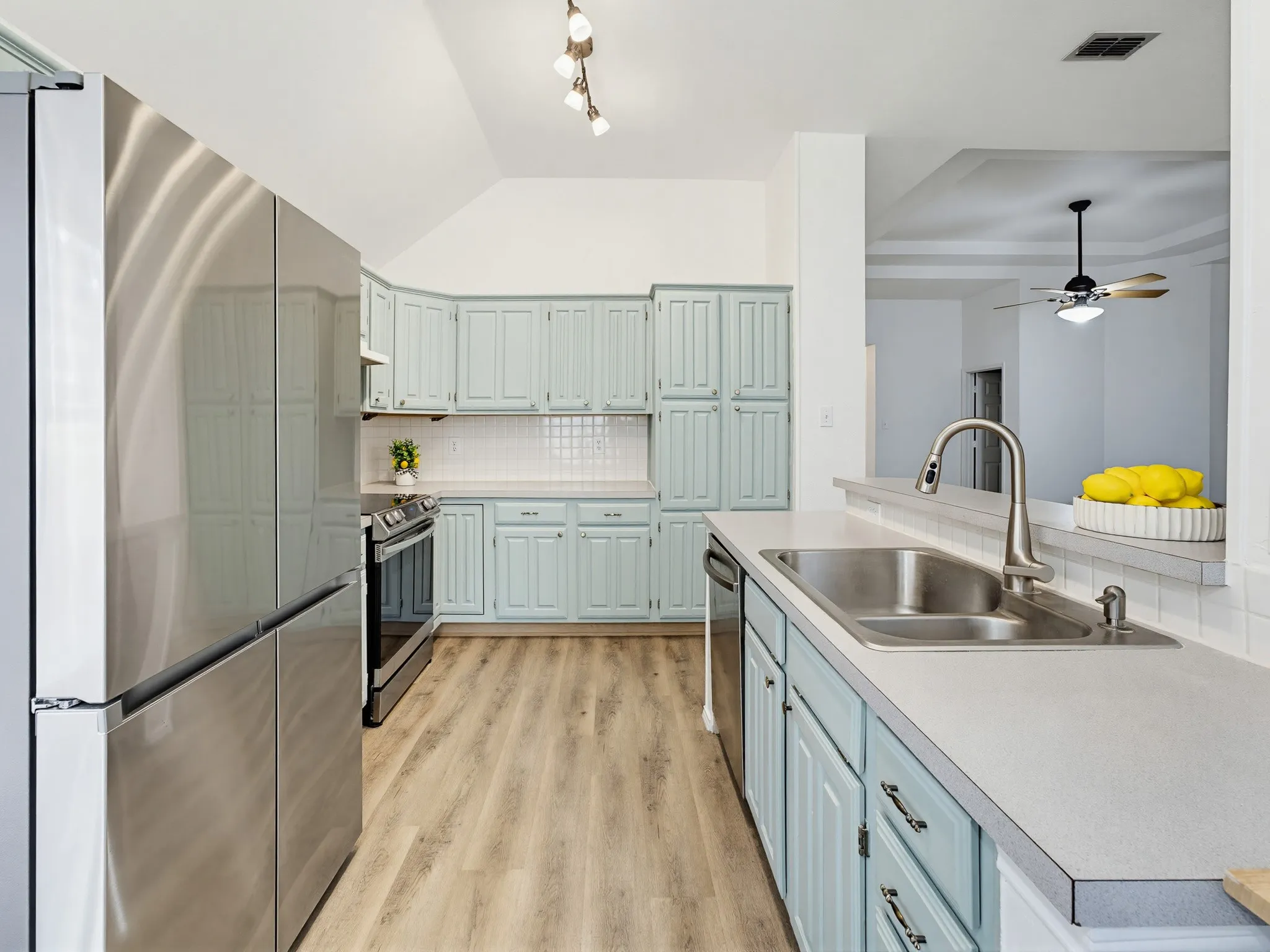 Kitchen featuring contemporary stainless steel appliances, light wood-finish flooring, light blue cabinetry with brushed nickel hardware, and a white subway tile backsplash