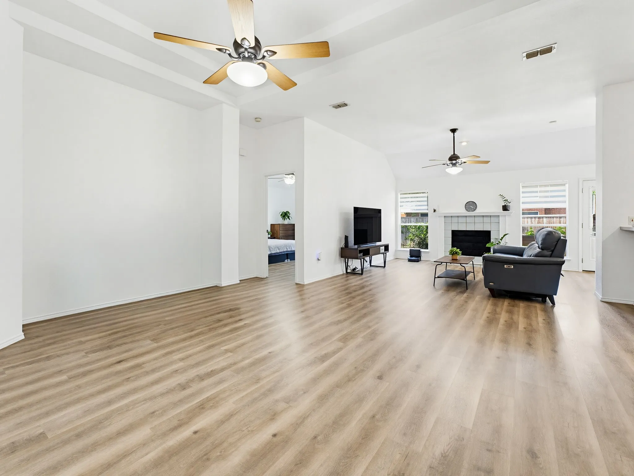Spacious open-concept living area featuring wood-finish flooring, vaulted ceilings, and ceiling fans
