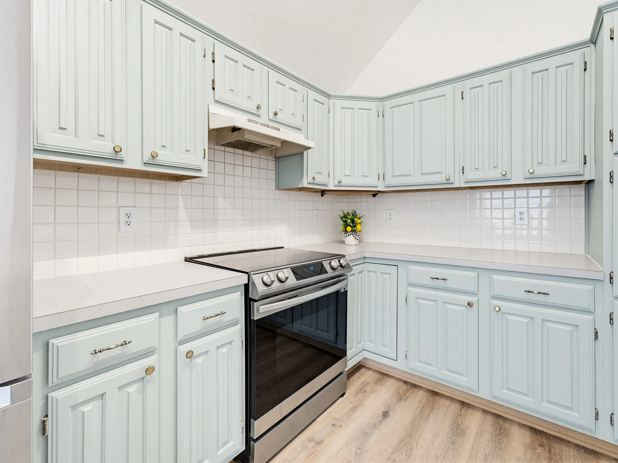 Kitchen featuring light blue cabinetry with gold-tone hardware, white tile backsplash, light-toned countertops, a stainless steel range, and wood-finish flooring