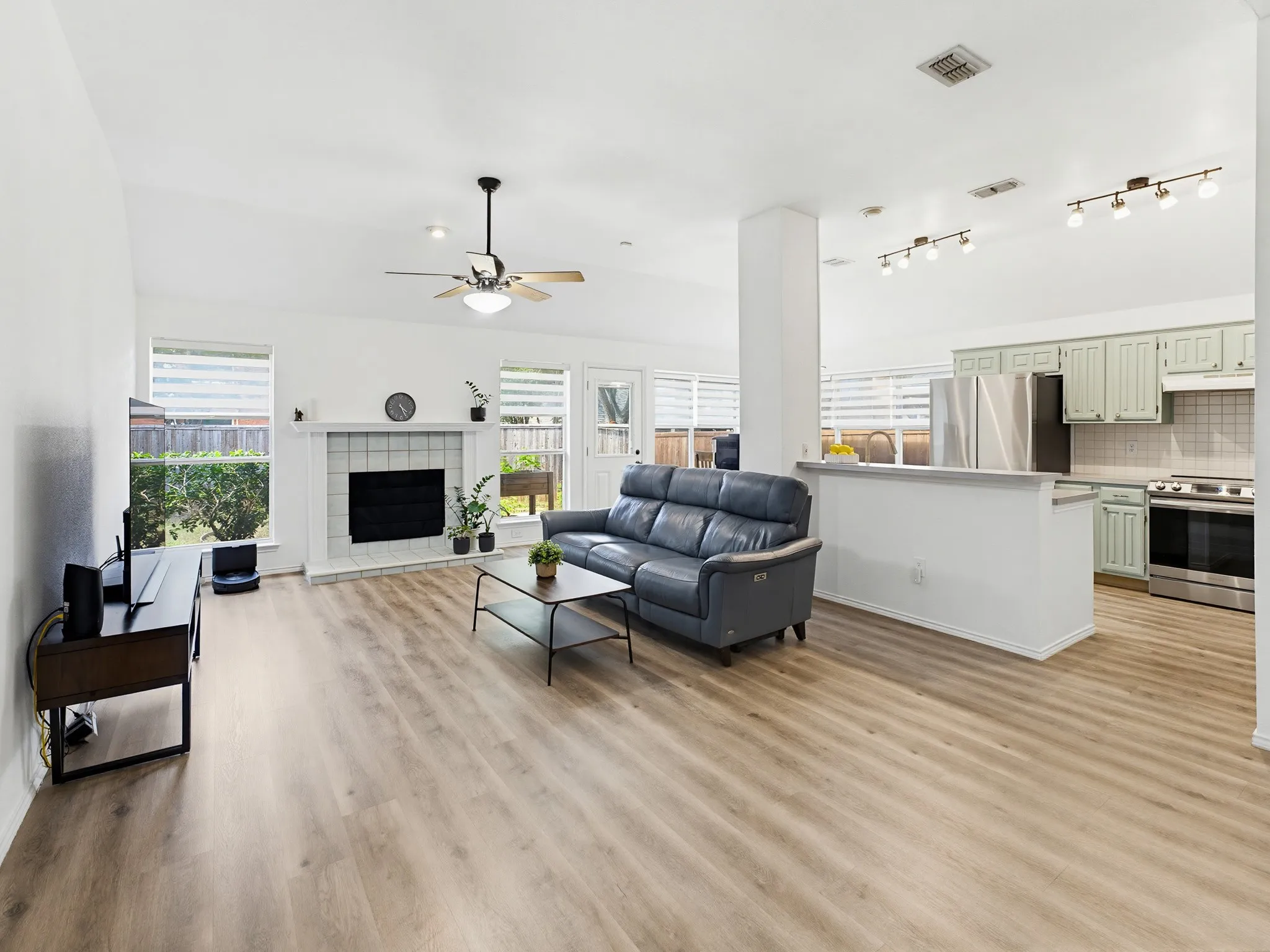 Open-concept living space featuring wood-finish flooring, a white-tiled fireplace with hearth, and a ceiling fan