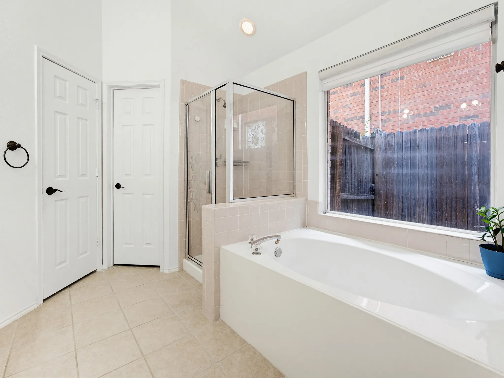 Spacious bathroom featuring a built-in soaking tub, a glass-enclosed shower, and light-toned tile flooring