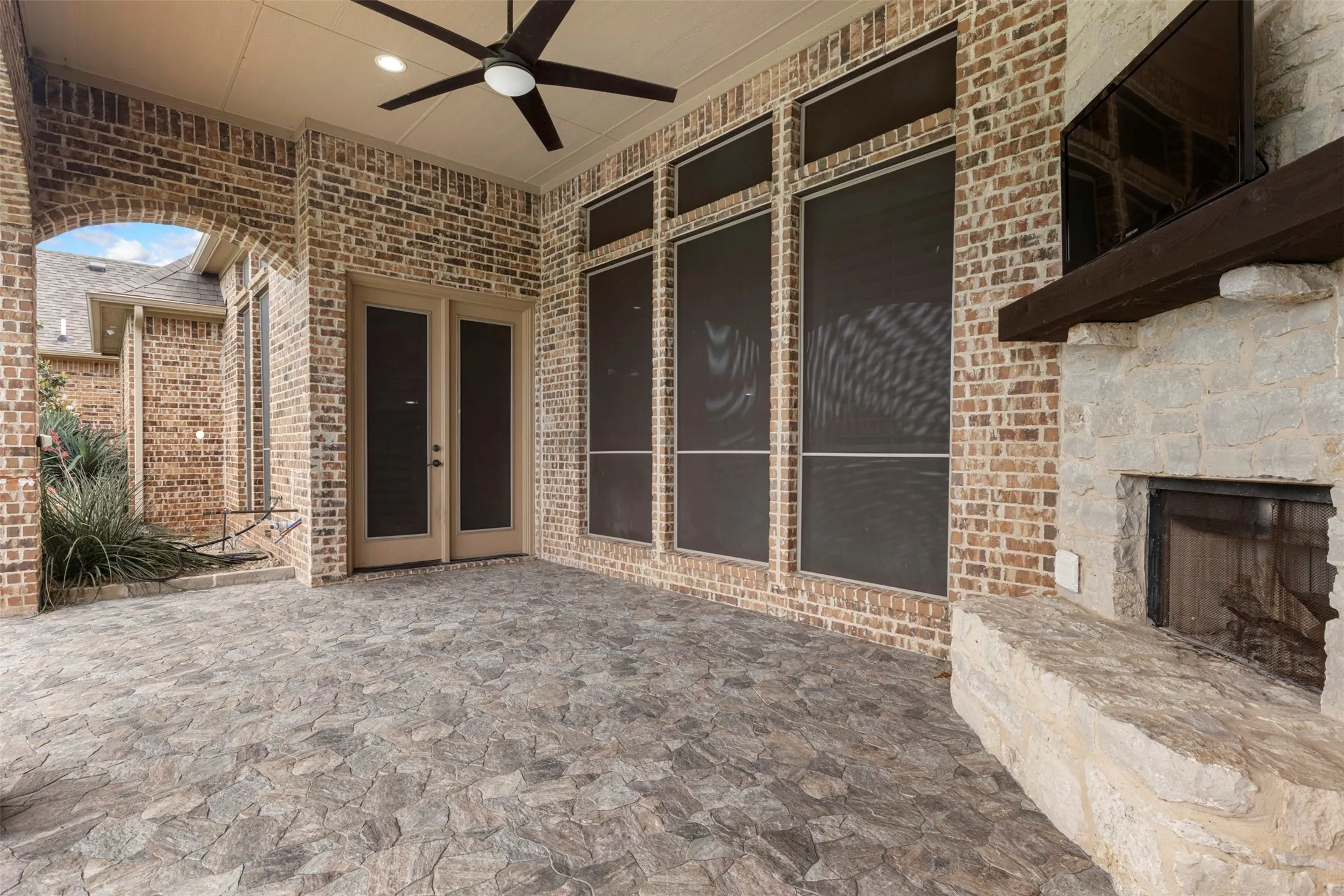 Expansive covered patio featuring a stone fireplace with a wood mantel, a large ceiling fan, and durable stone​​‌​​​​‌​​‌‌​‌‌​​​‌‌​‌​‌​‌​​​‌​​ flooring