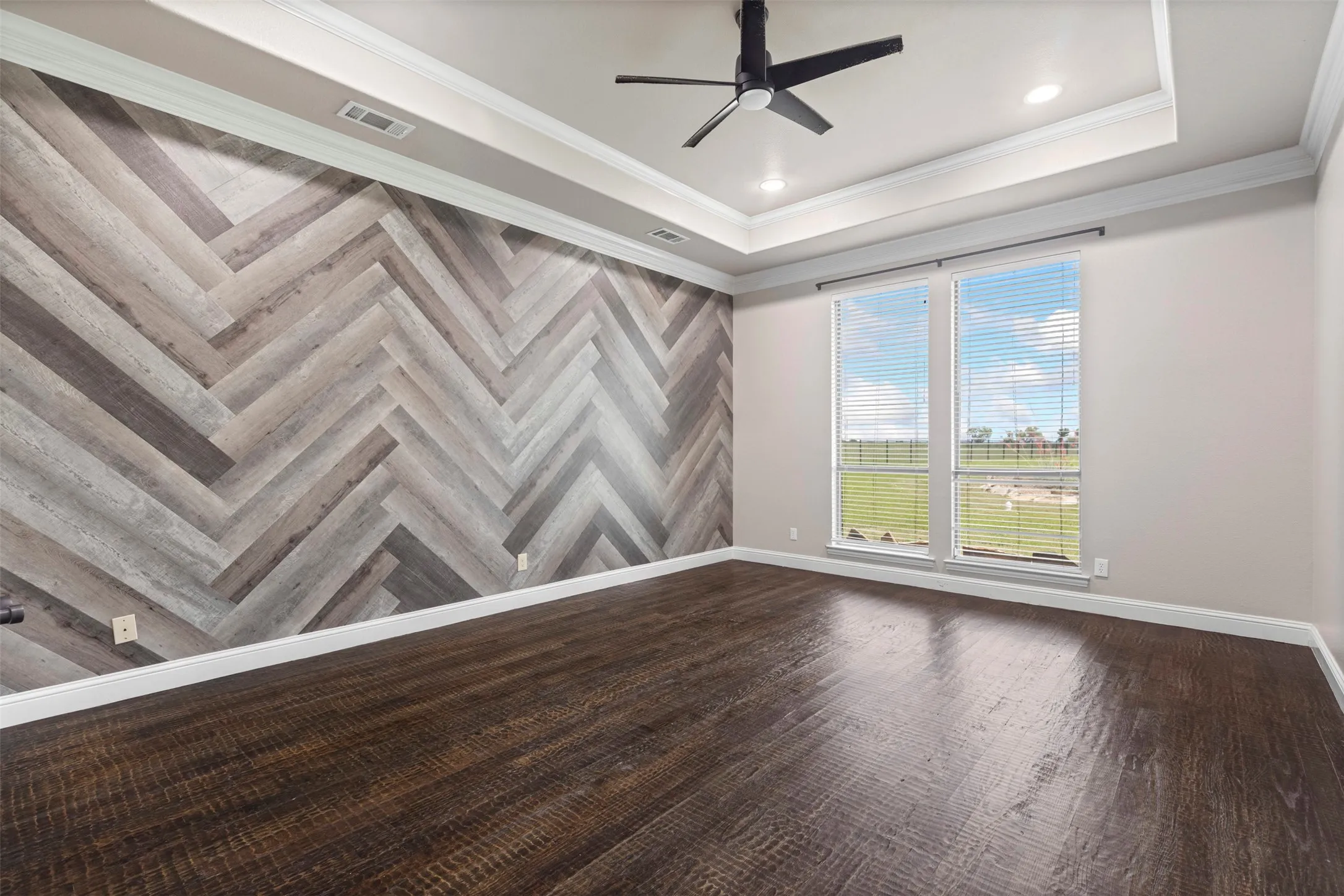 Feature wall with a herringbone wood-finish pattern, tray ceiling with recessed lighting, dark wood-finish flooring, and a ceiling fan