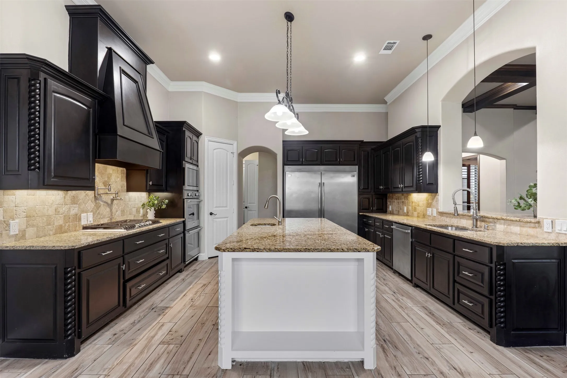 Gourmet kitchen featuring dark wood cabinetry, light granite countertops, tile backsplash, stainless steel appliances, and a central island with pendant lighting