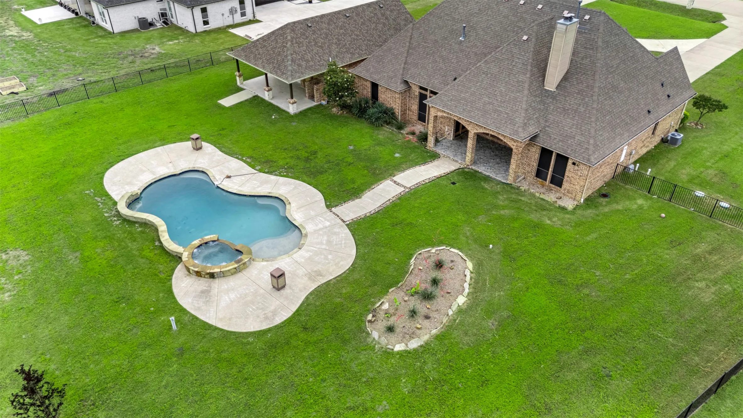 Expansive backyard featuring a freeform swimming pool with integrated spa, concrete patio surround, and a defined planting bed