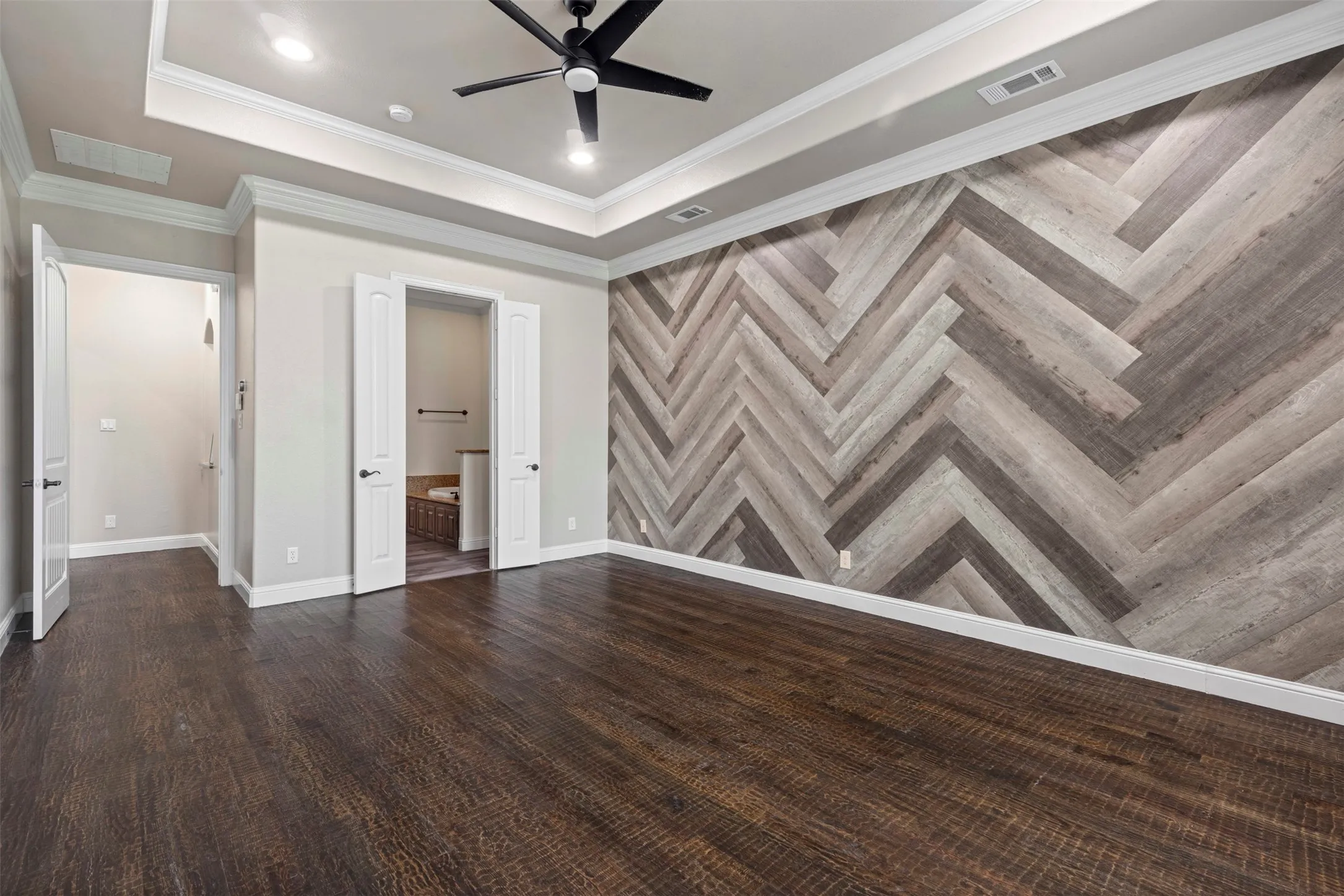 Interior room featuring a herringbone pattern accent wall, dark wood-finish flooring, and a tray ceiling with recessed lighting