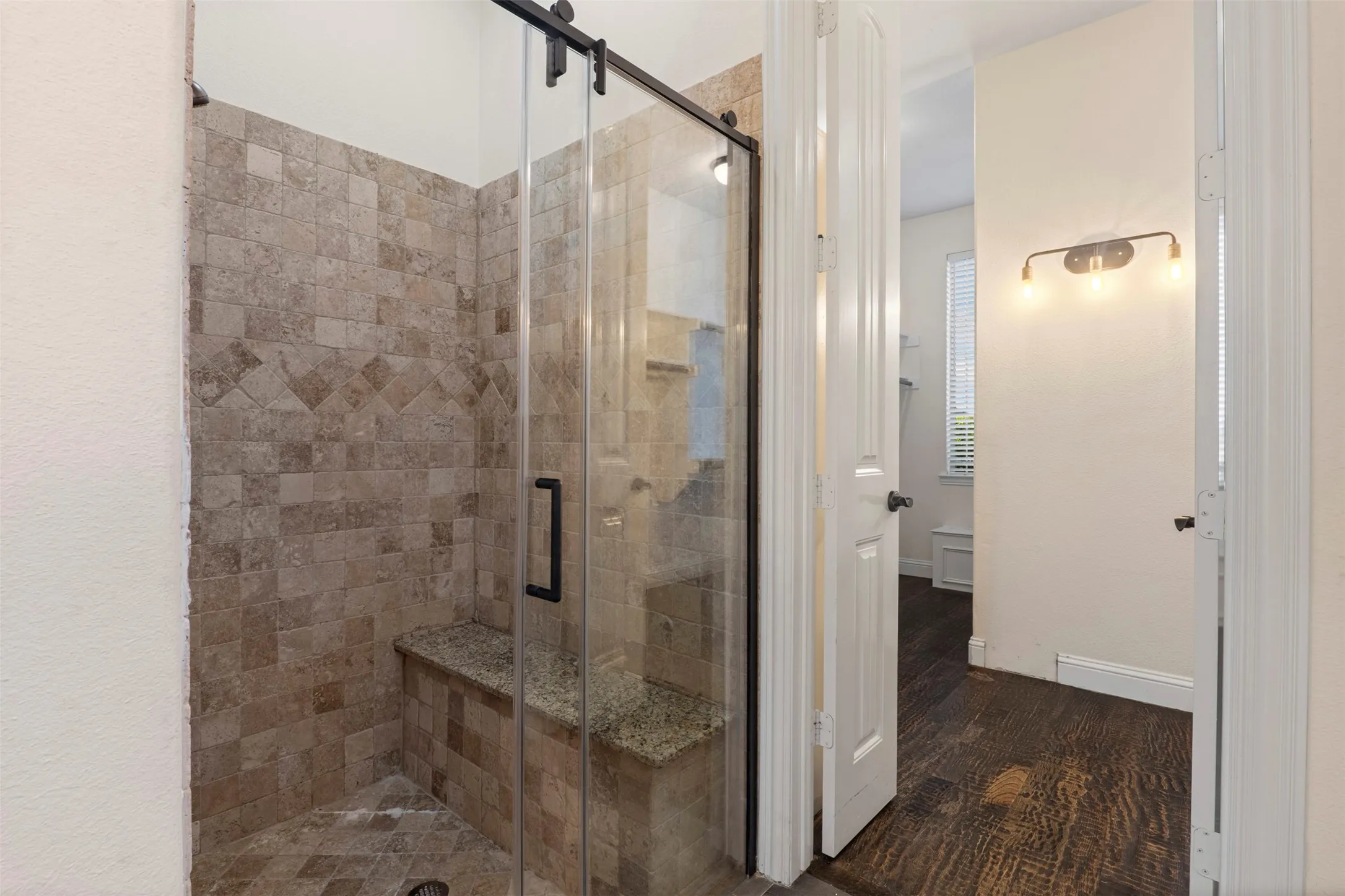 Glass-enclosed shower with stone tile surround and integrated bench seating