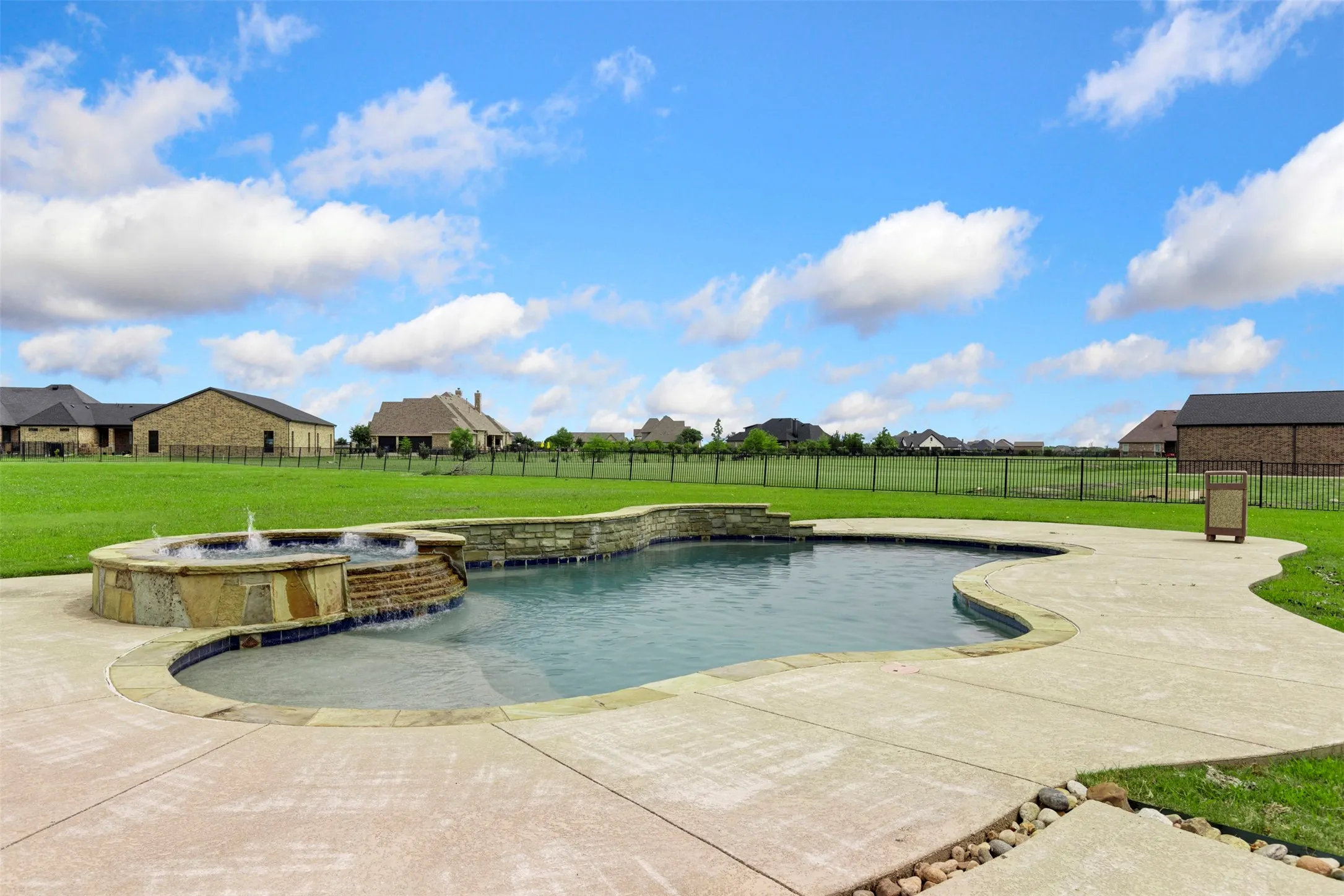 Freeform swimming pool featuring a built-in spa with water feature, stone coping, and a surrounding concrete deck
