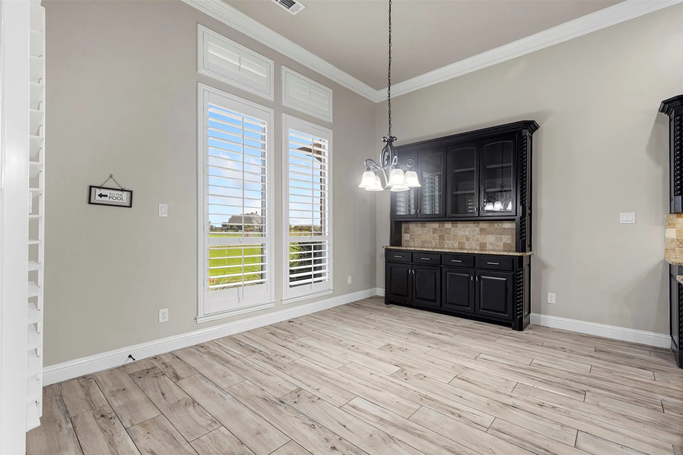 Dining area featuring high ceilings with crown molding, wood-finish flooring, and a built-in black cabinetry unit with a stone tile backsplash