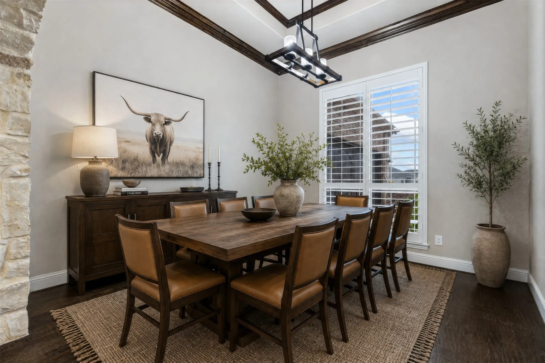 Spacious dining area featuring dark wood-finish flooring, a tray ceiling with dark wood beams, and a rectangular window with plantation shutters