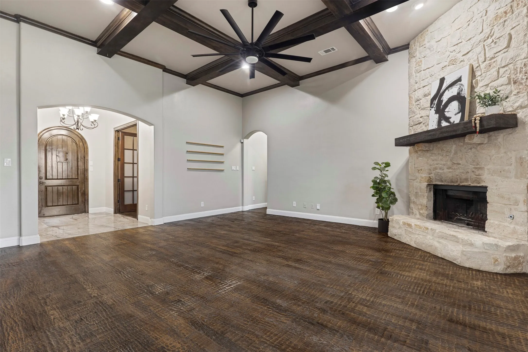 Spacious living area featuring exposed wood beams, a stone fireplace with a substantial wood mantel, and wood-finish flooring
