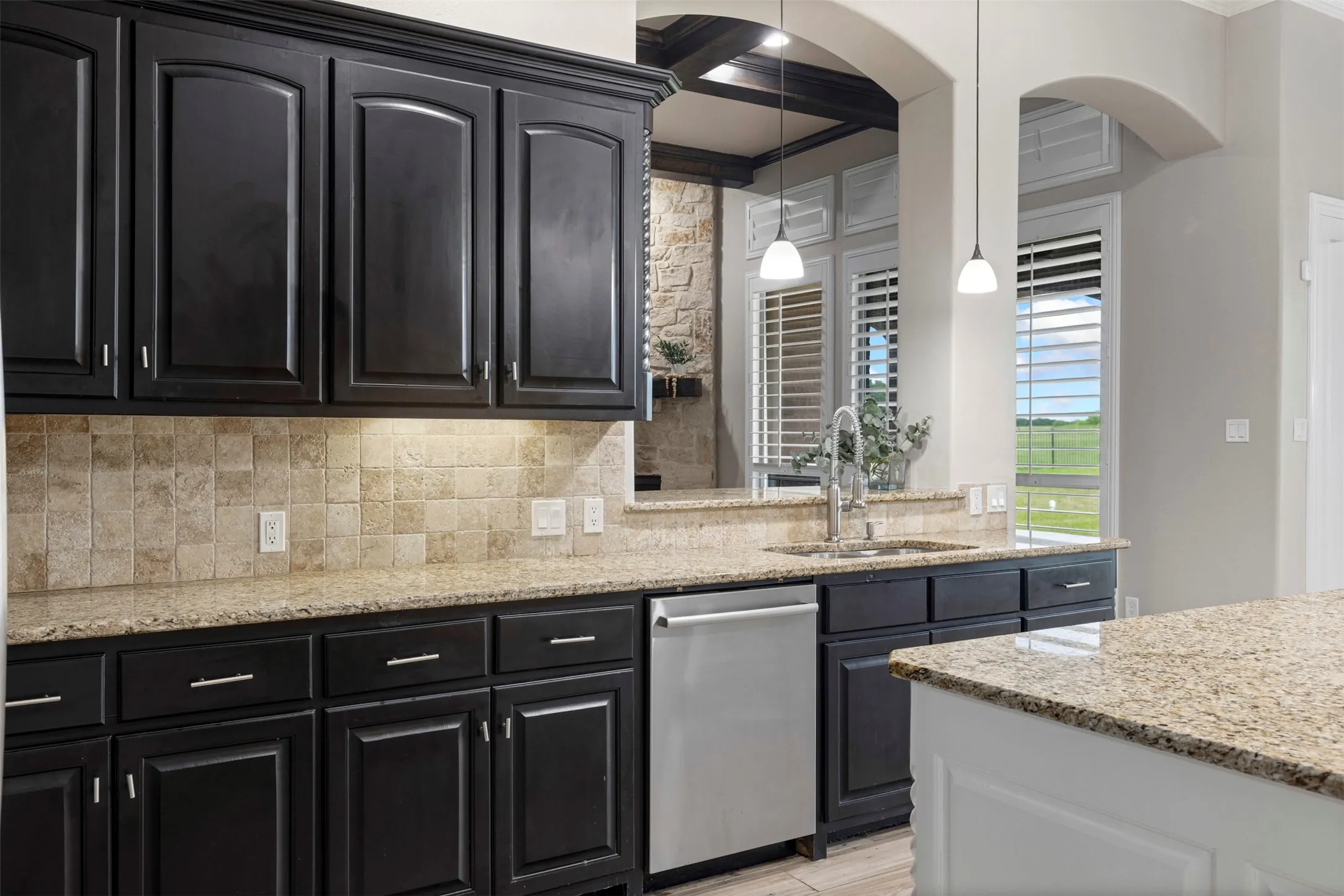 Kitchen featuring dark cabinetry with brushed nickel hardware, stone-finish countertops, a tiled backsplash, and stainless steel dishwasher