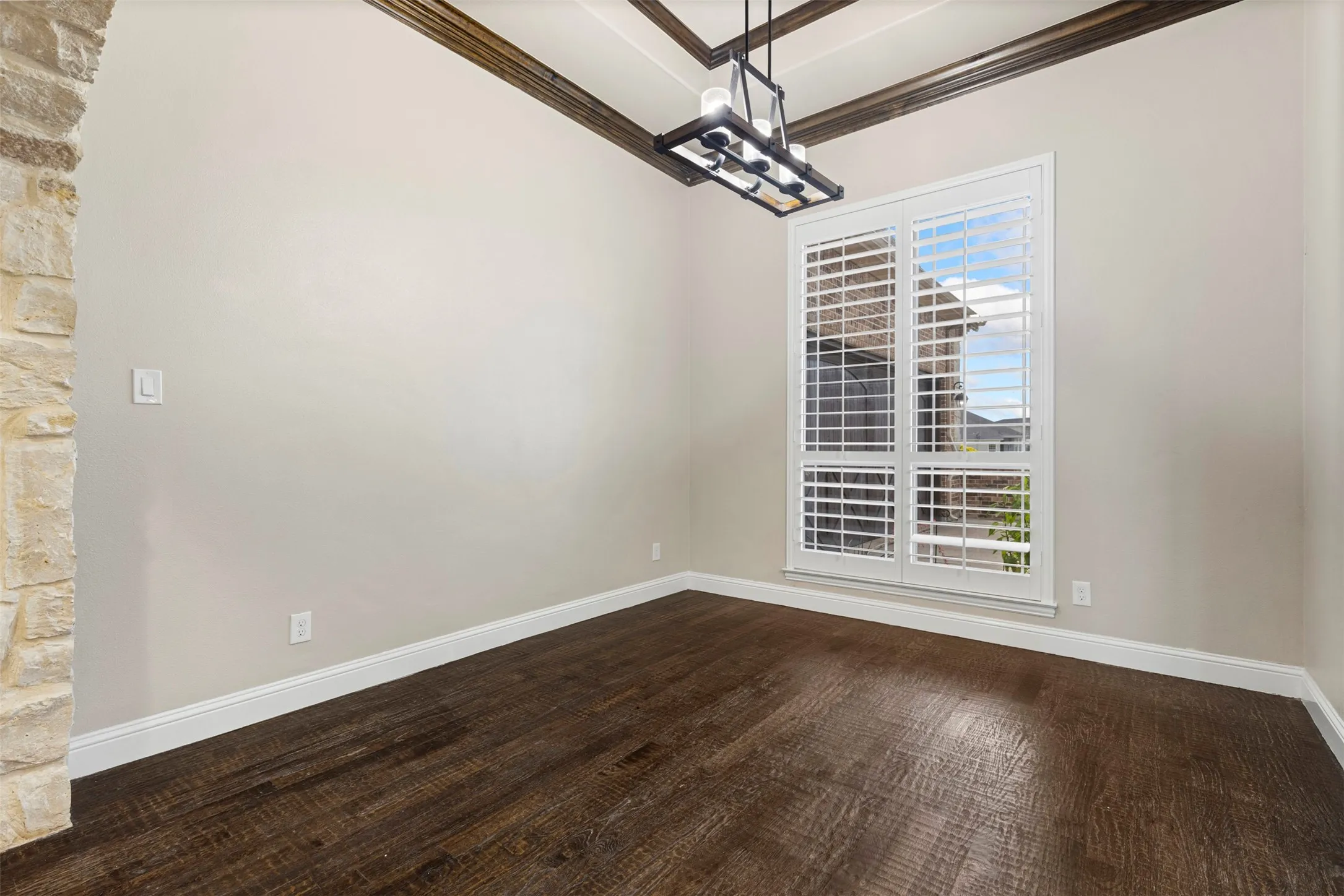 Spacious room featuring dark wood-finish flooring, a stone-accented wall, and a large window with plantation shutters