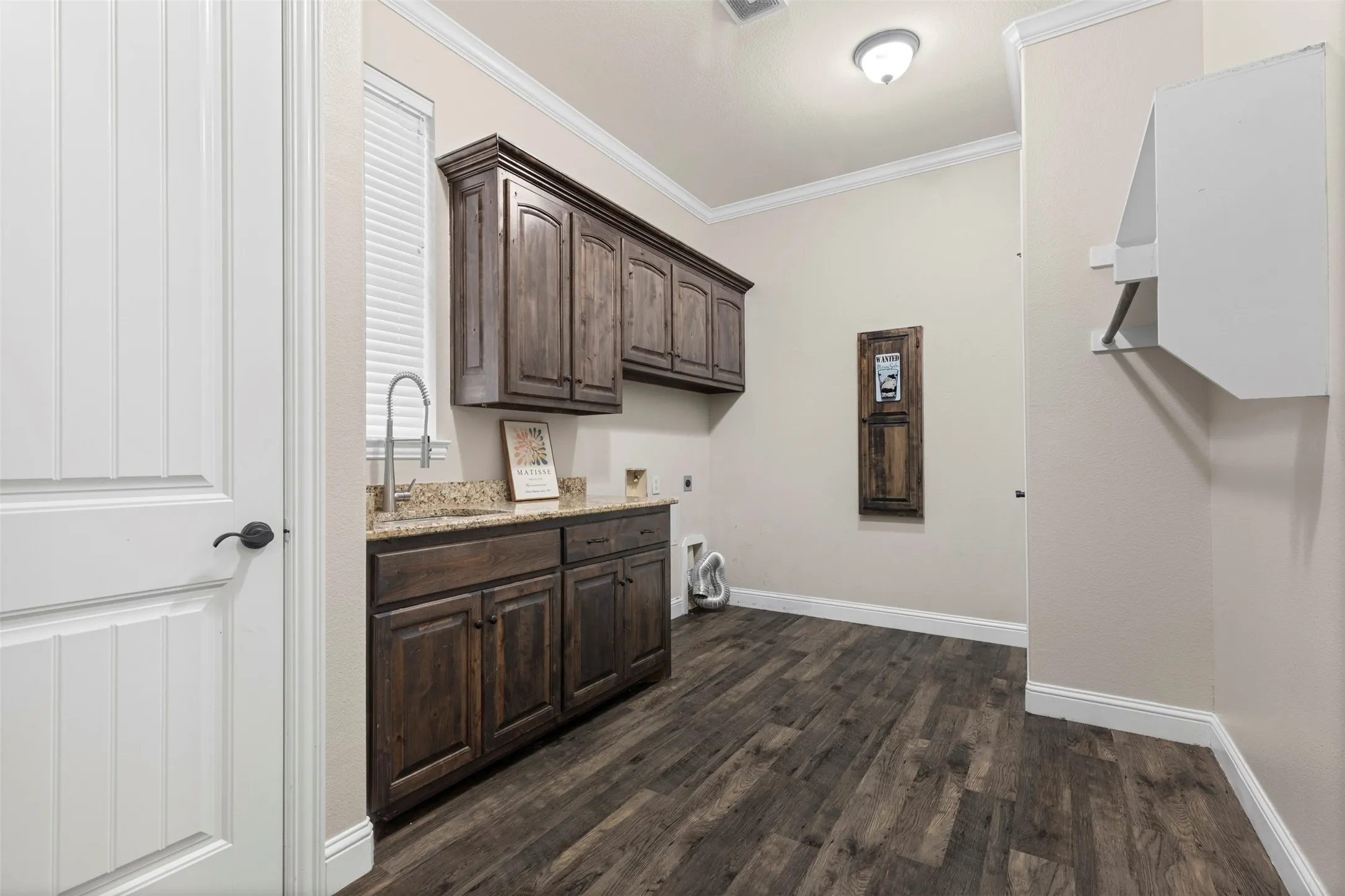 Utility room with rich wood-finish cabinetry, granite-style countertop, and stainless steel sink