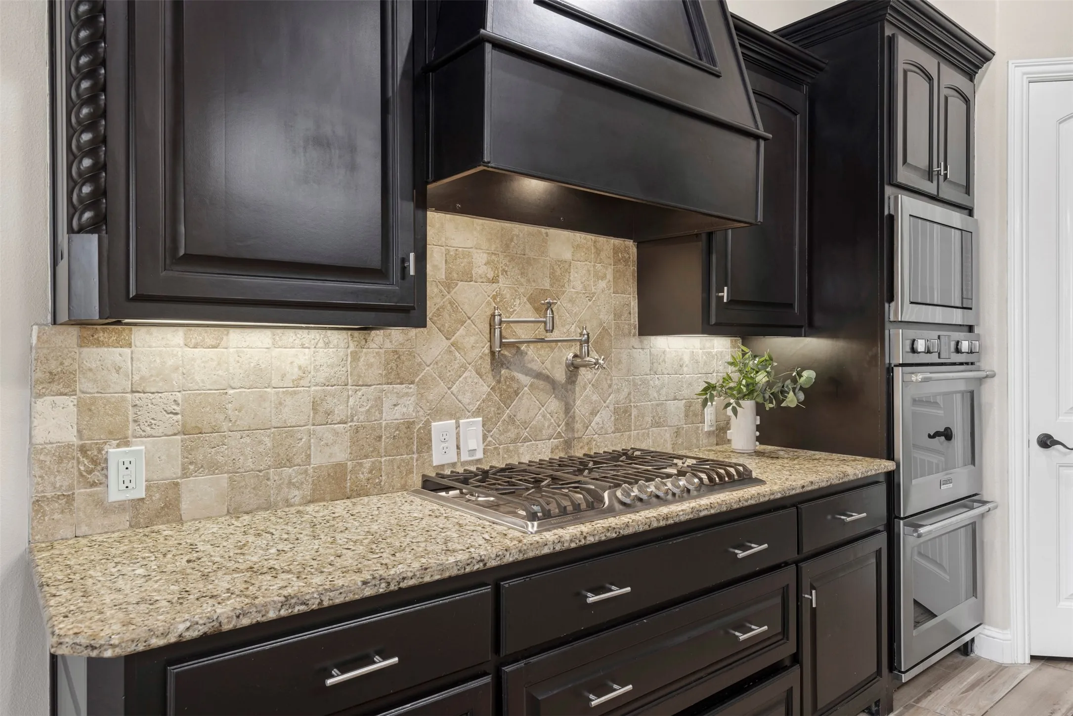 Kitchen featuring dark wood cabinetry, a gas cooktop, granite countertops, a tiled backsplash, and stainless steel double ovens