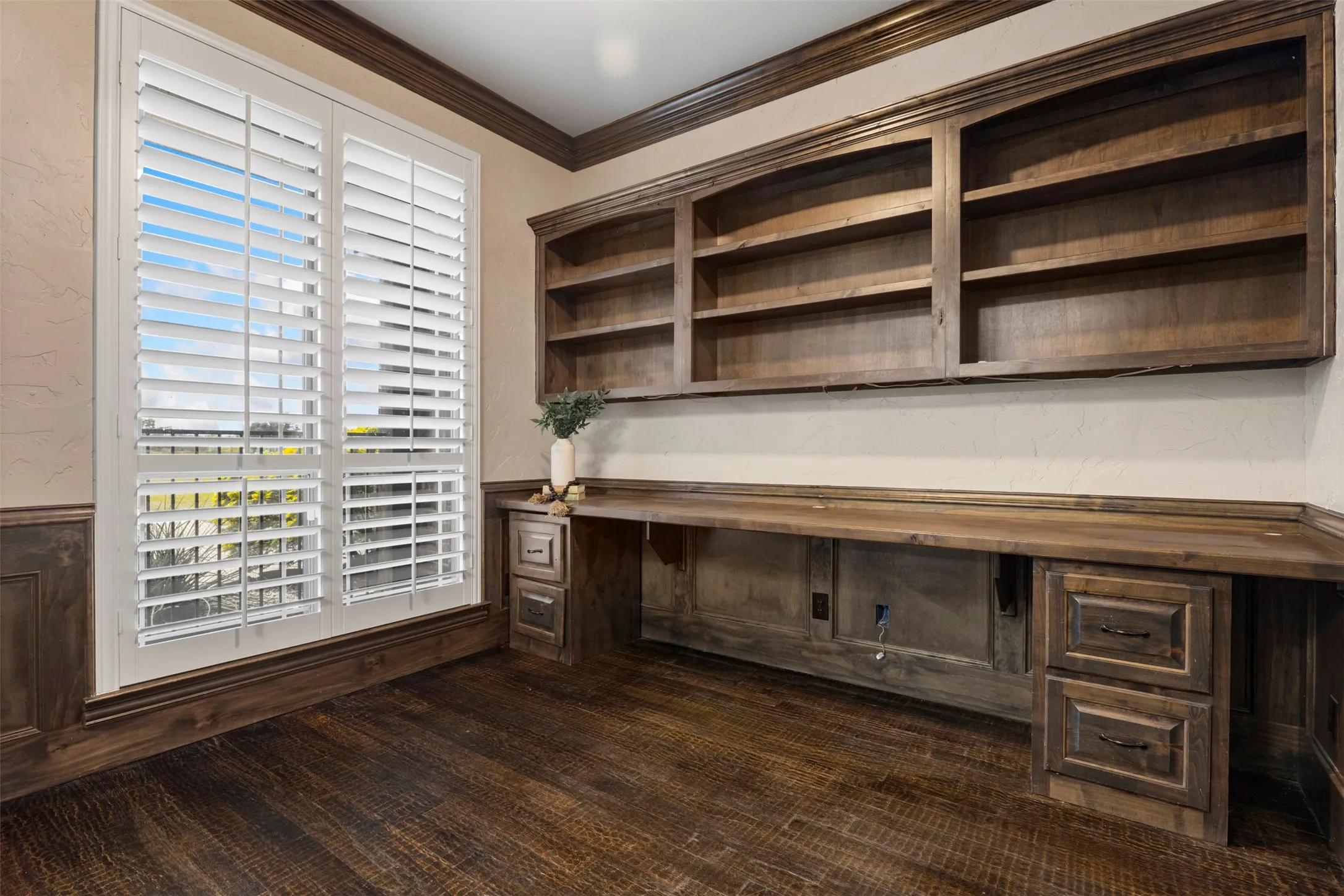 Custom built-in desk with integrated shelving, dark wood-finish flooring, and white plantation shutters