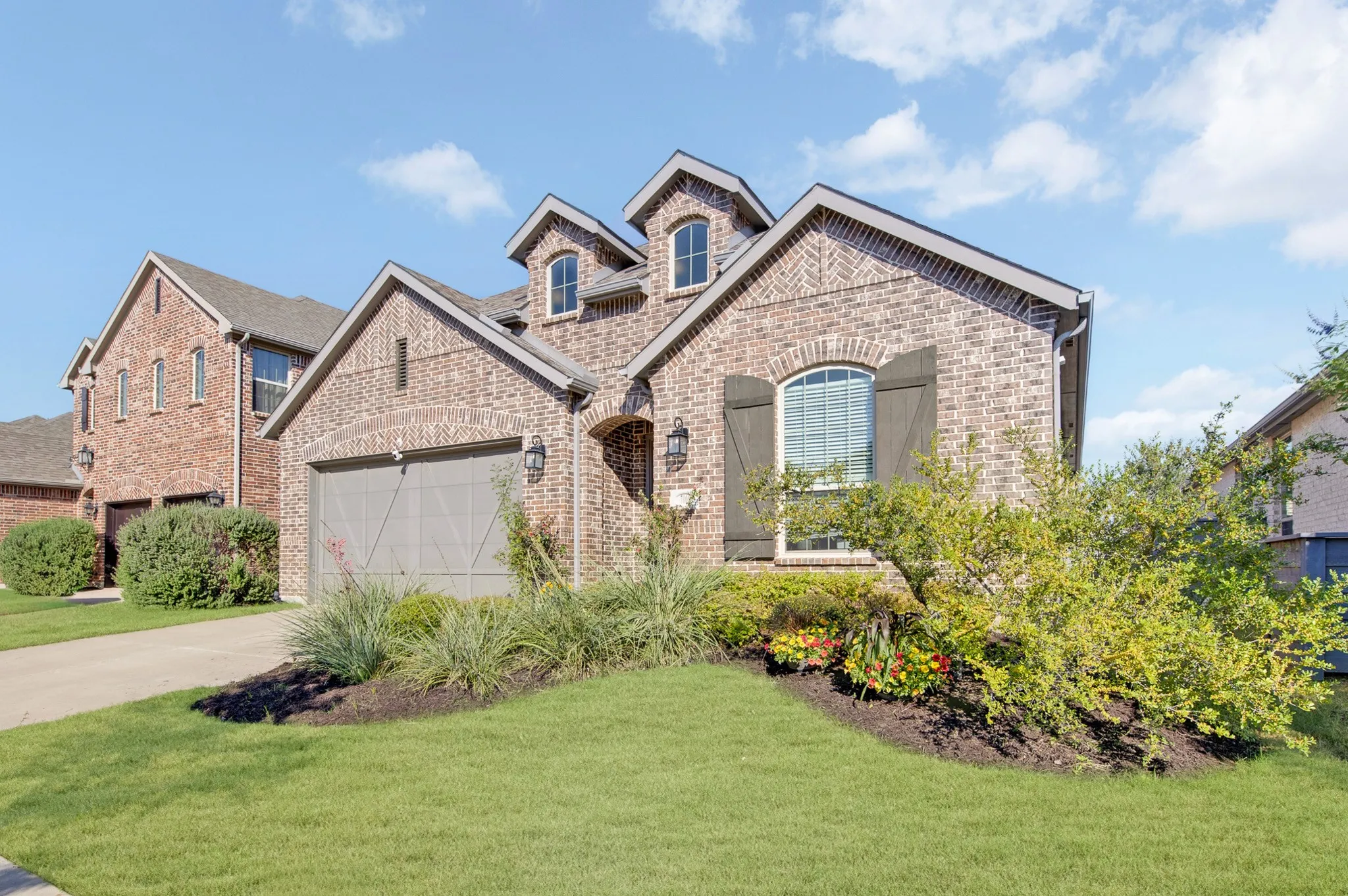 Brick Colonial featuring a two-car garage with carriage-style doors, arched entry with transom window, and multiple gables with dormer windows