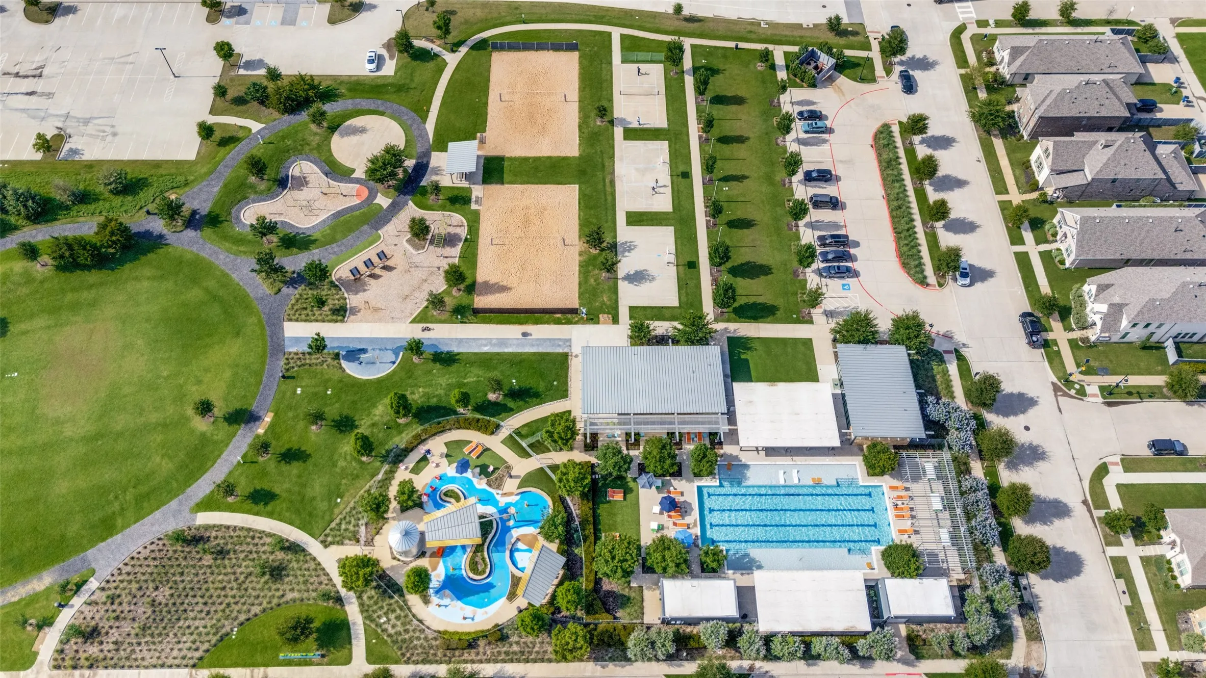 Aerial perspective showcasing extensive community amenities, including a multi-lane swimming pool, recreational water park, multiple sand volleyball courts, and children's playground areas