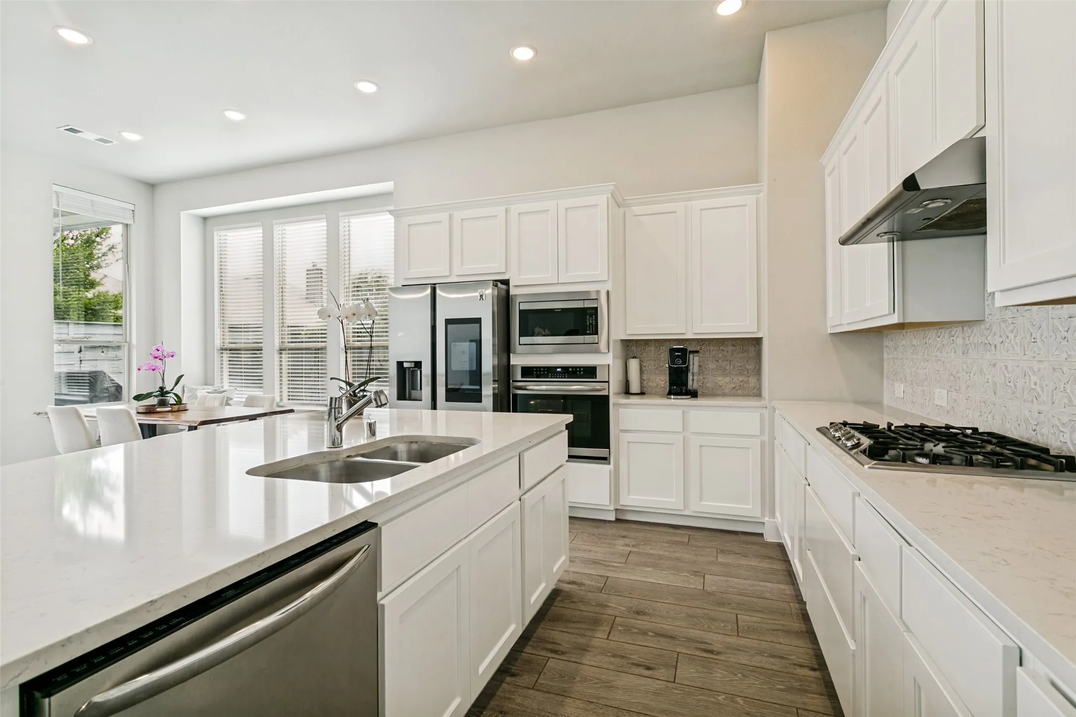 Gourmet kitchen featuring a center island with double sink, white cabinetry, integrated stainless steel appliances, wood-finish flooring, and recessed lighting