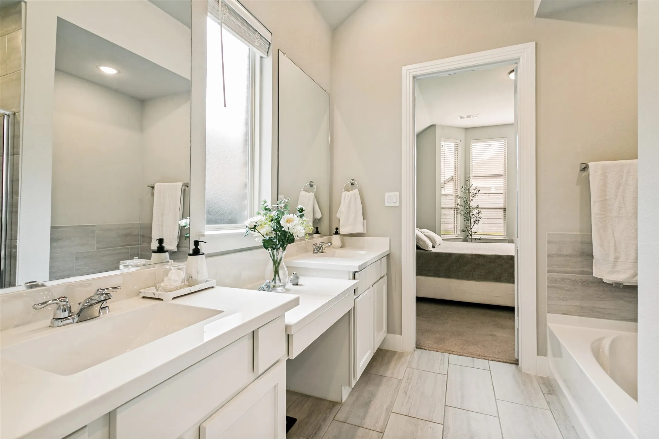 Bathroom featuring a double vanity with integrated sinks and white countertops, large mirrors, built-in bathtub, and rectangular tile flooring