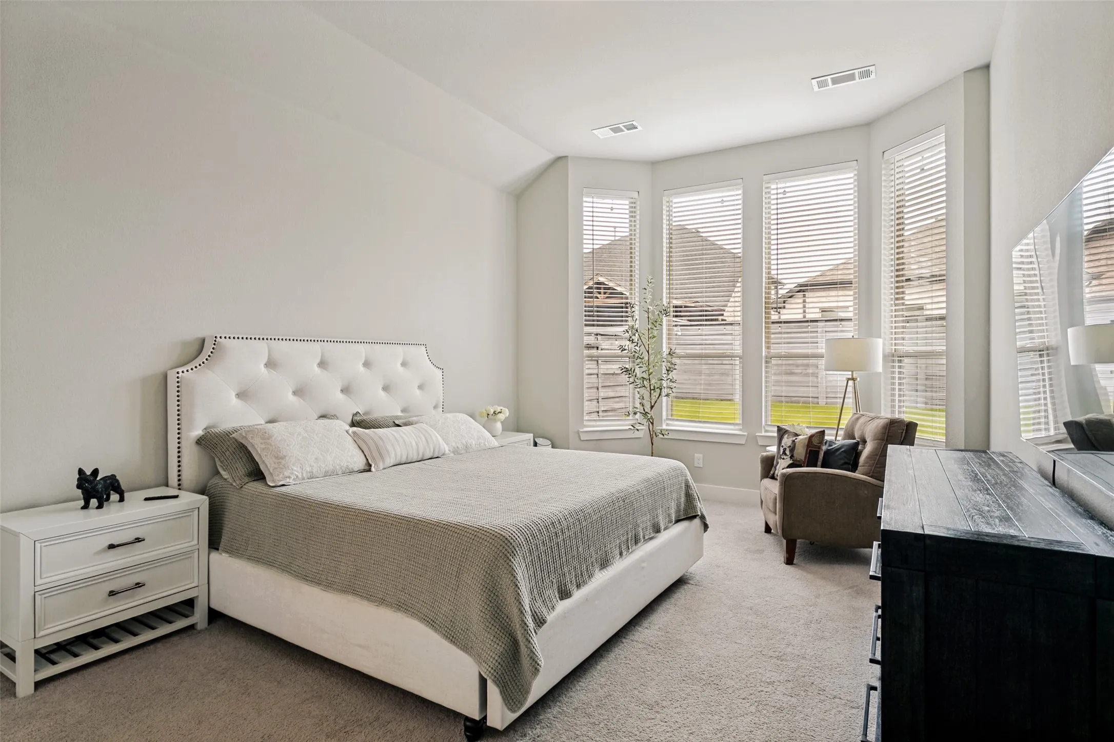Bright bedroom featuring a bay window with multiple vertical windows, light-colored walls, and neutral carpet flooring