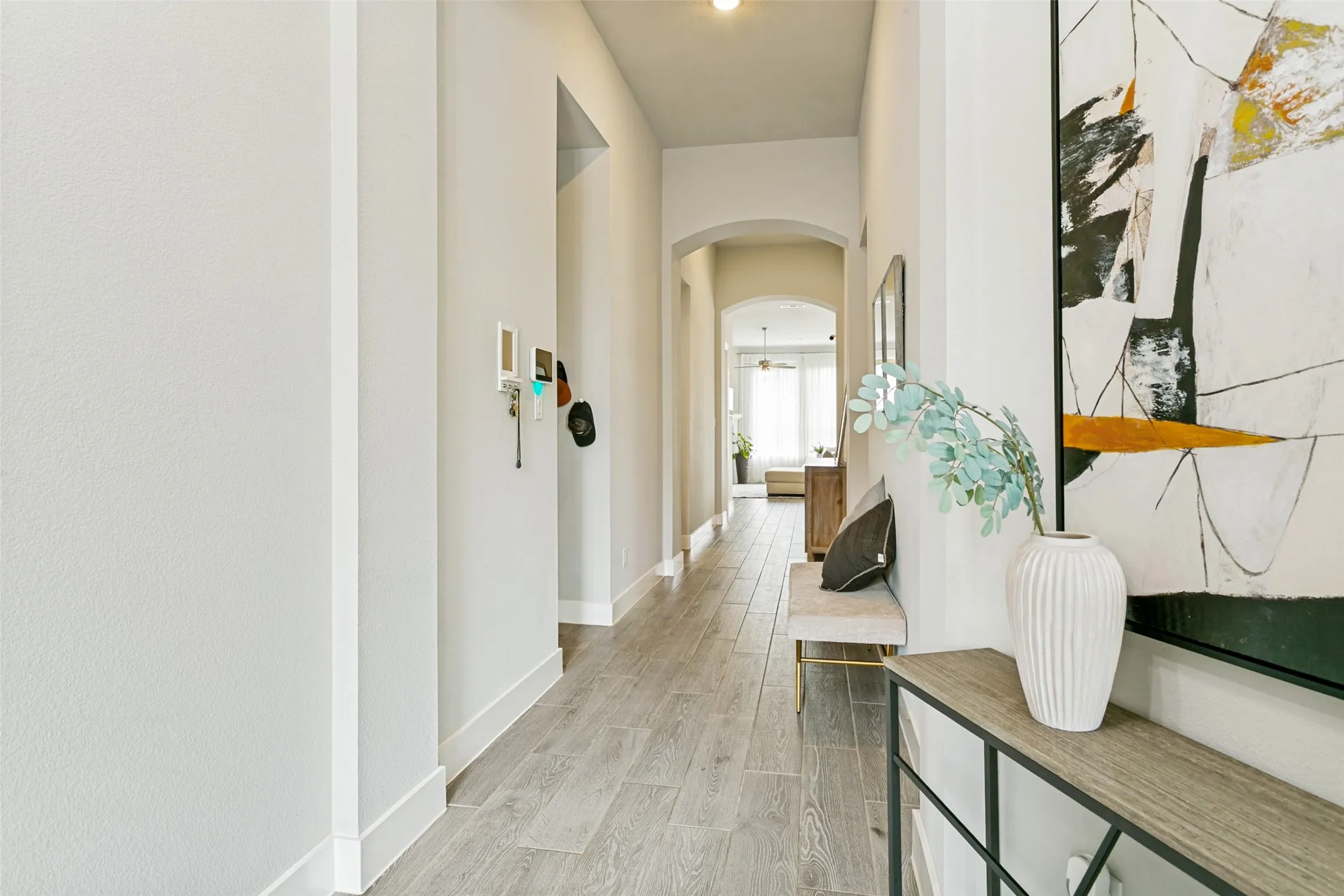 Bright hallway featuring wood-finish flooring, light neutral paint, and an arched entryway