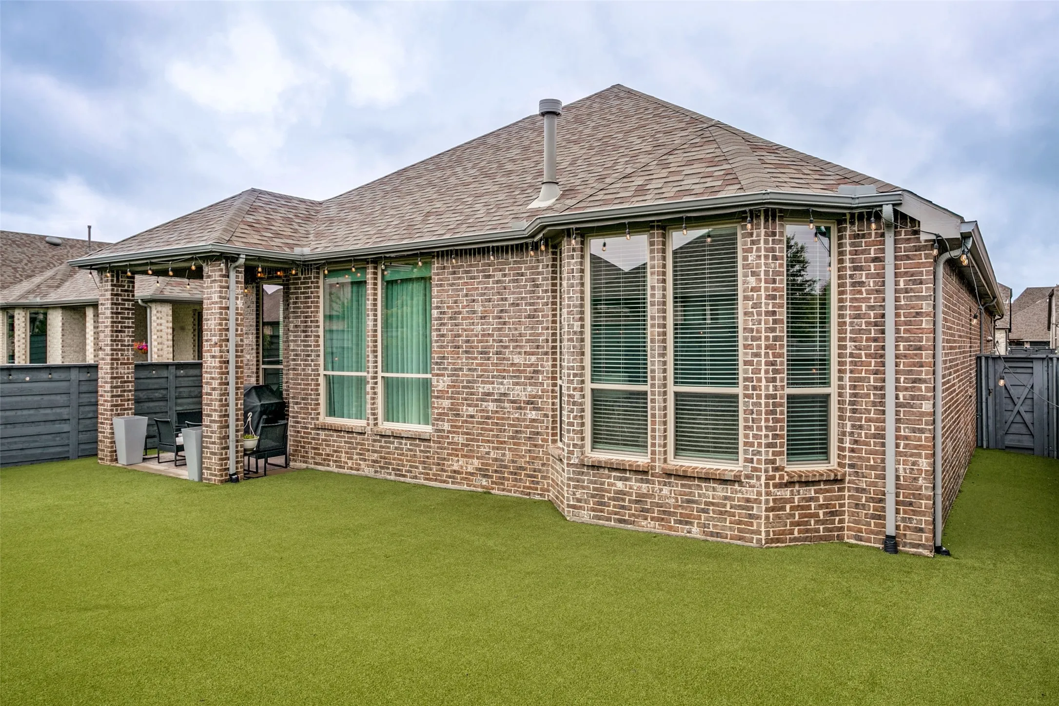 Rear exterior featuring brick facade, bay windows, and a covered patio with a concrete slab