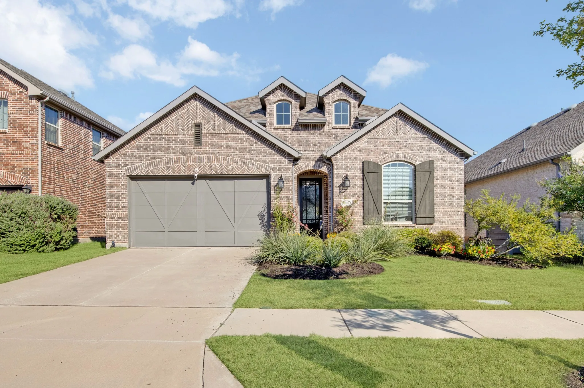 Elegant brick and stone facade featuring arched entry, decorative dormer windows, and a three-car garage with X-panel detailing