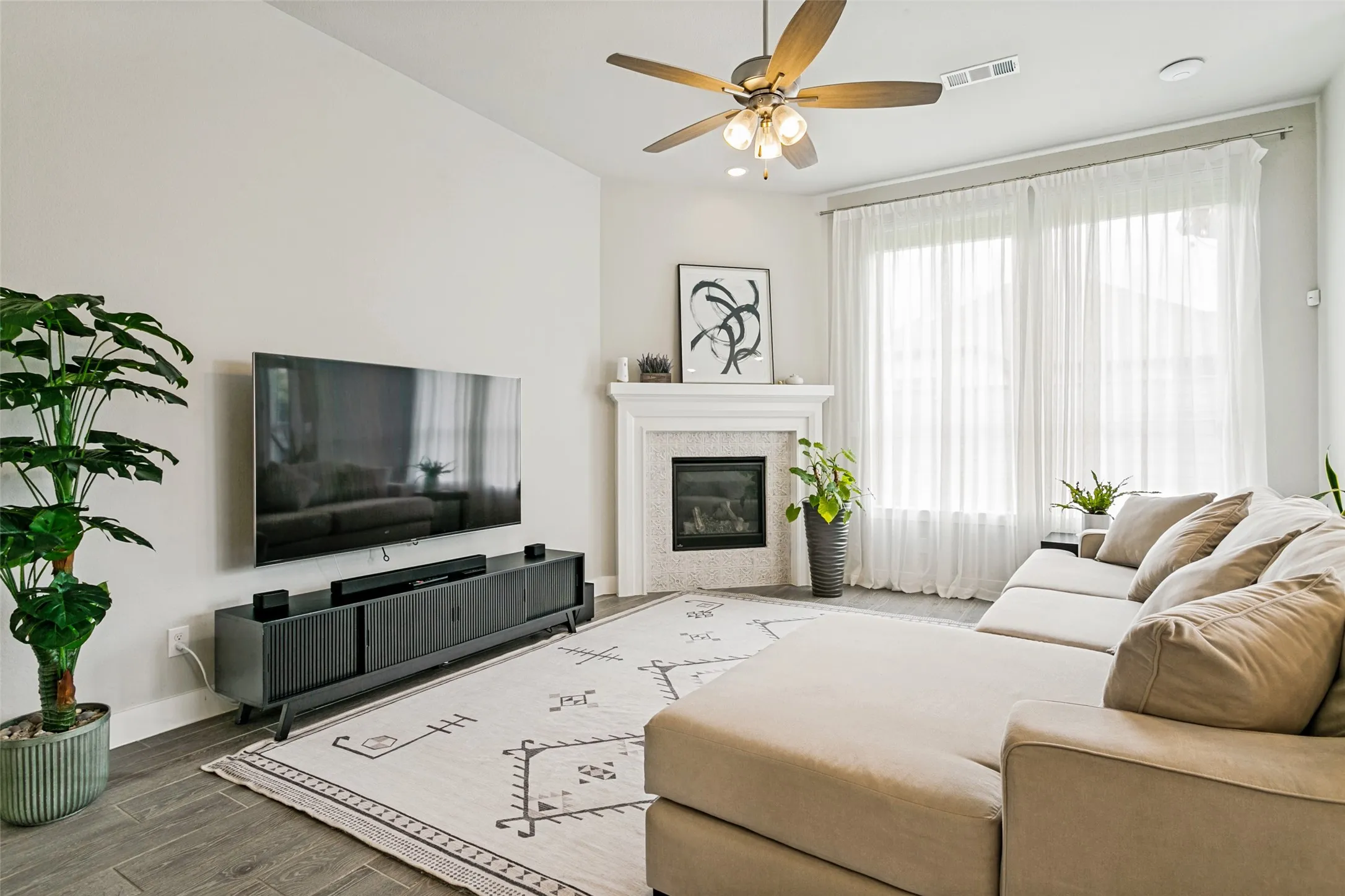 Living area featuring wood-finish flooring, a ceiling fan, and a corner fireplace with a white mantel and mosaic tile surround