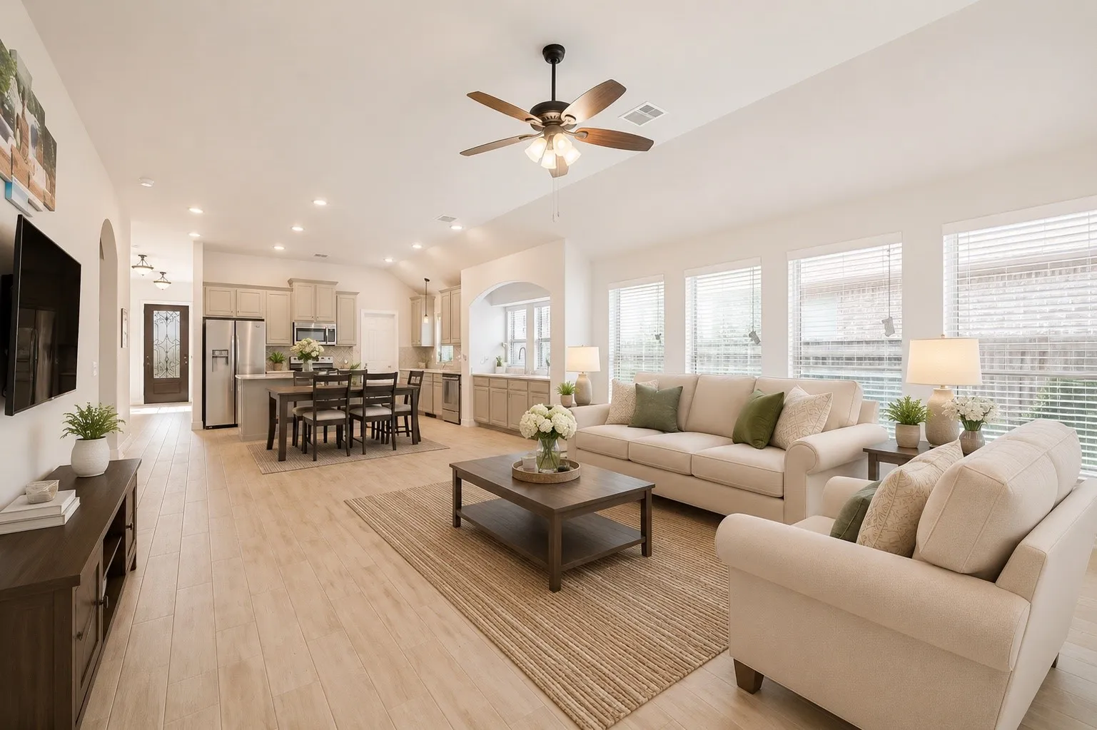 Open-concept living space featuring wood-finish flooring, vaulted ceilings, recessed lighting, and multiple windows with blinds