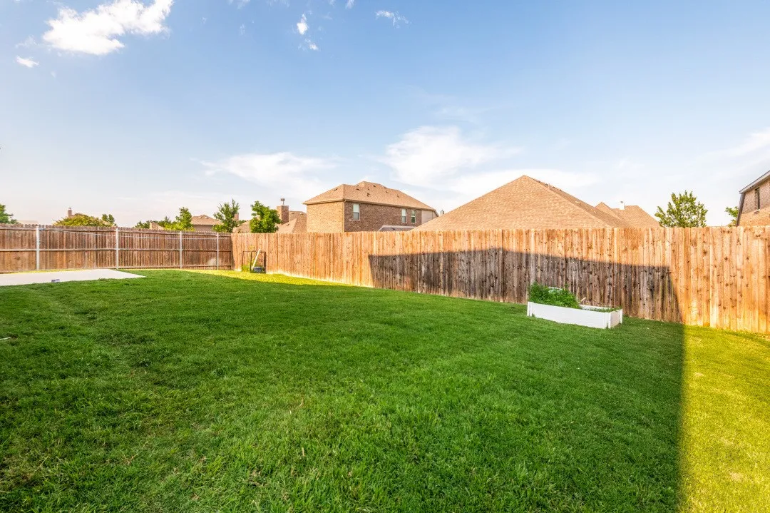 Spacious backyard featuring a large grass lawn, wood privacy fencing, and a concrete patio pad