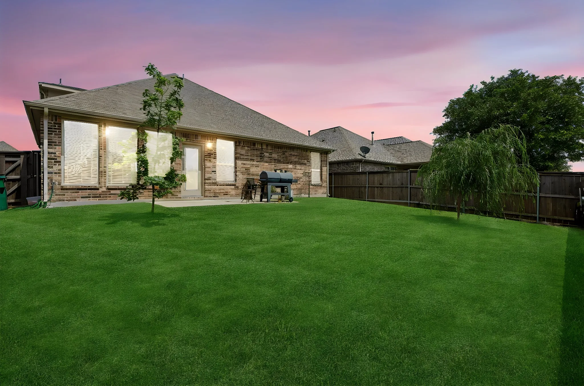 Expansive backyard featuring a lush lawn, mature trees, and a wooden privacy fence