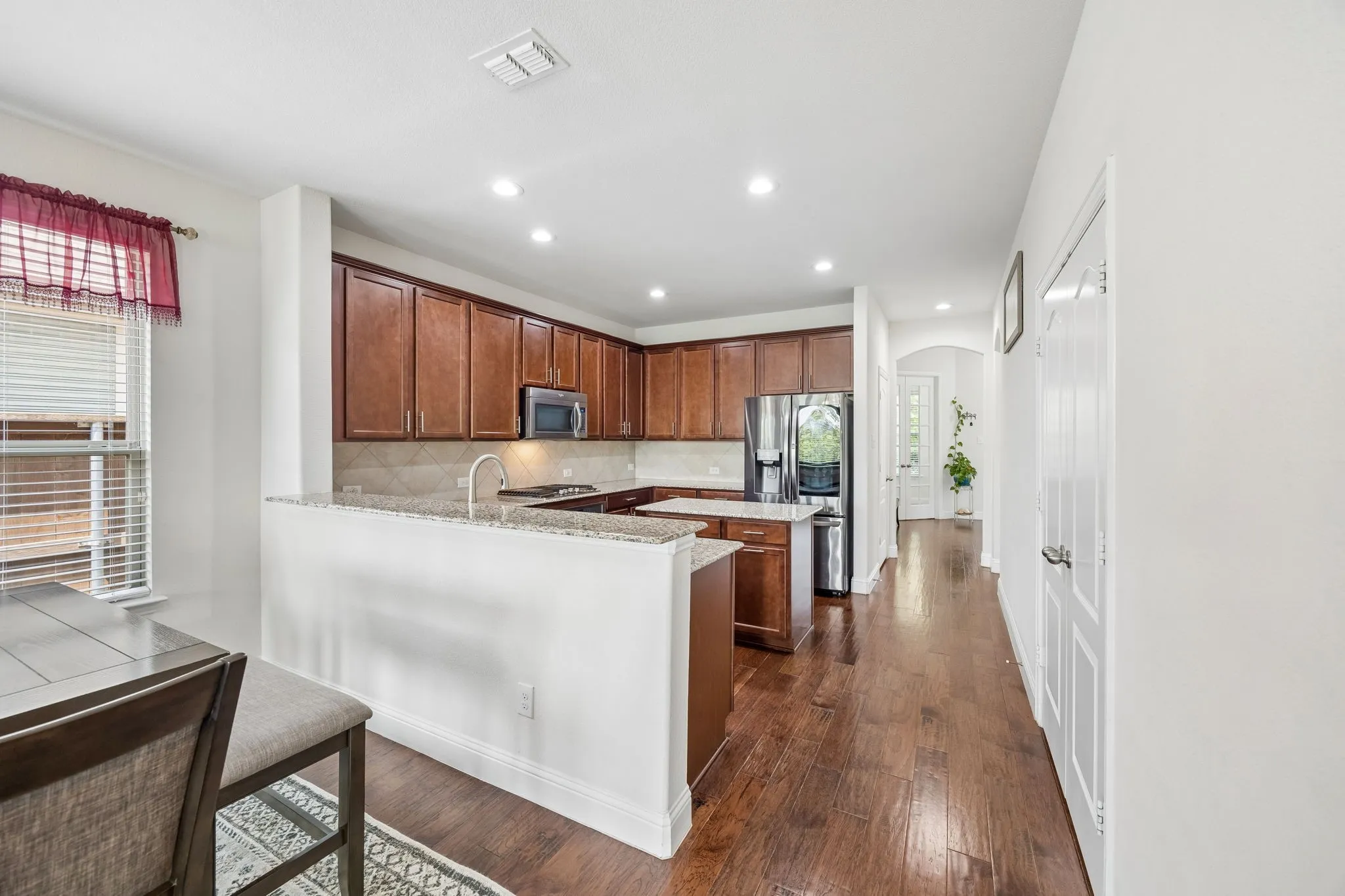 Kitchen featuring wood flooring, granite countertops, wood cabinetry, stainless steel appliances, and an island with additional counter space
