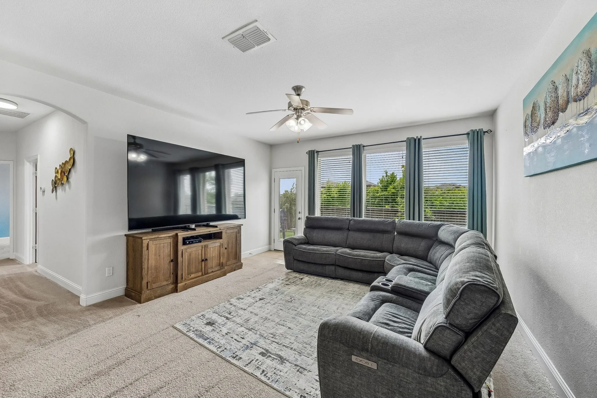 Living room with a ceiling fan and wall of windows overlooking the back yard.
