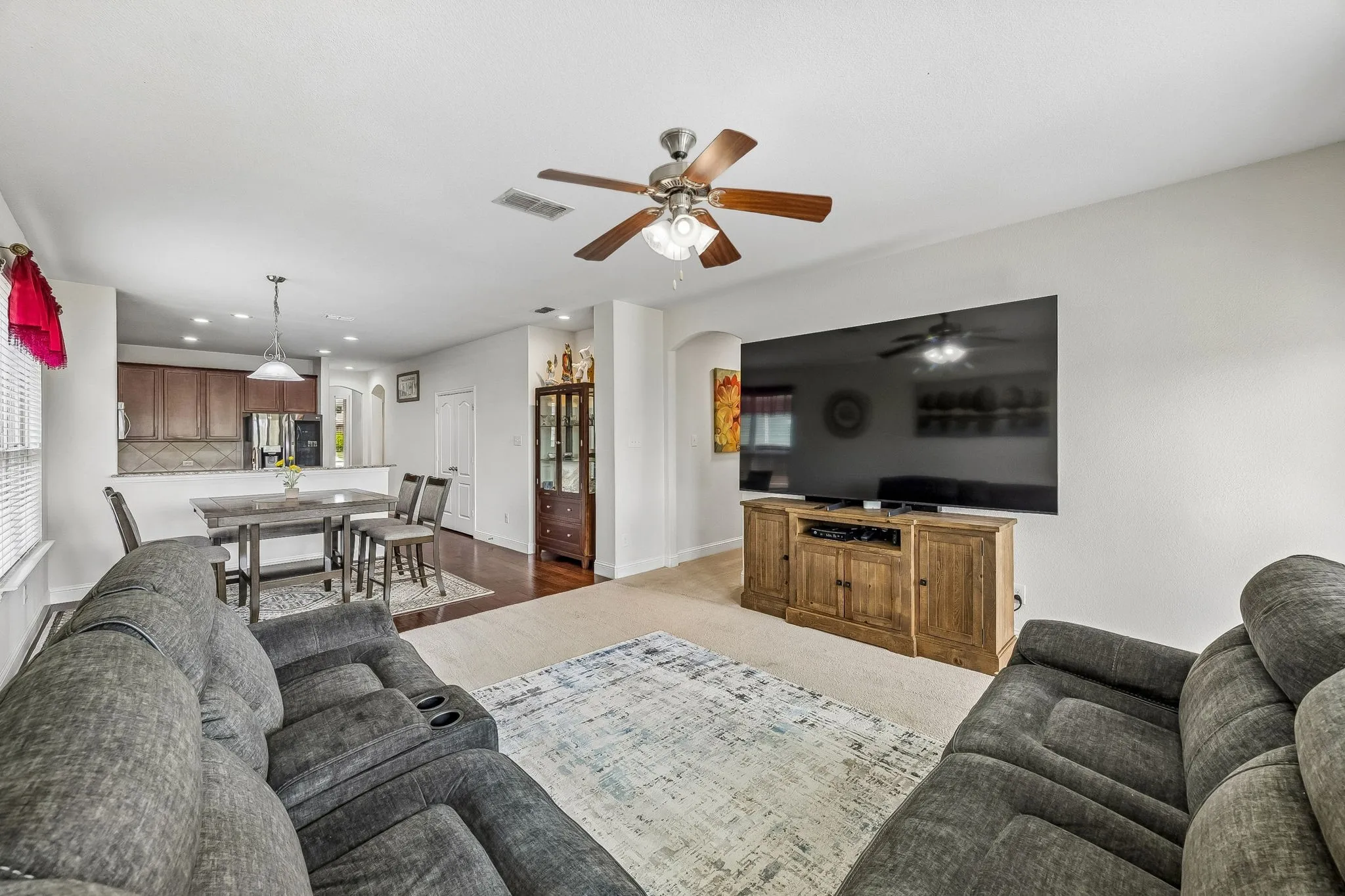 Open-concept living area with light-toned carpeting and a ceiling fan