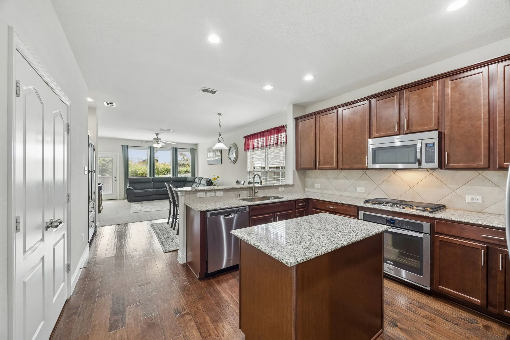 Kitchen featuring wood flooring, granite countertops, wood cabinetry, stainless steel appliances, and an island with additional counter space