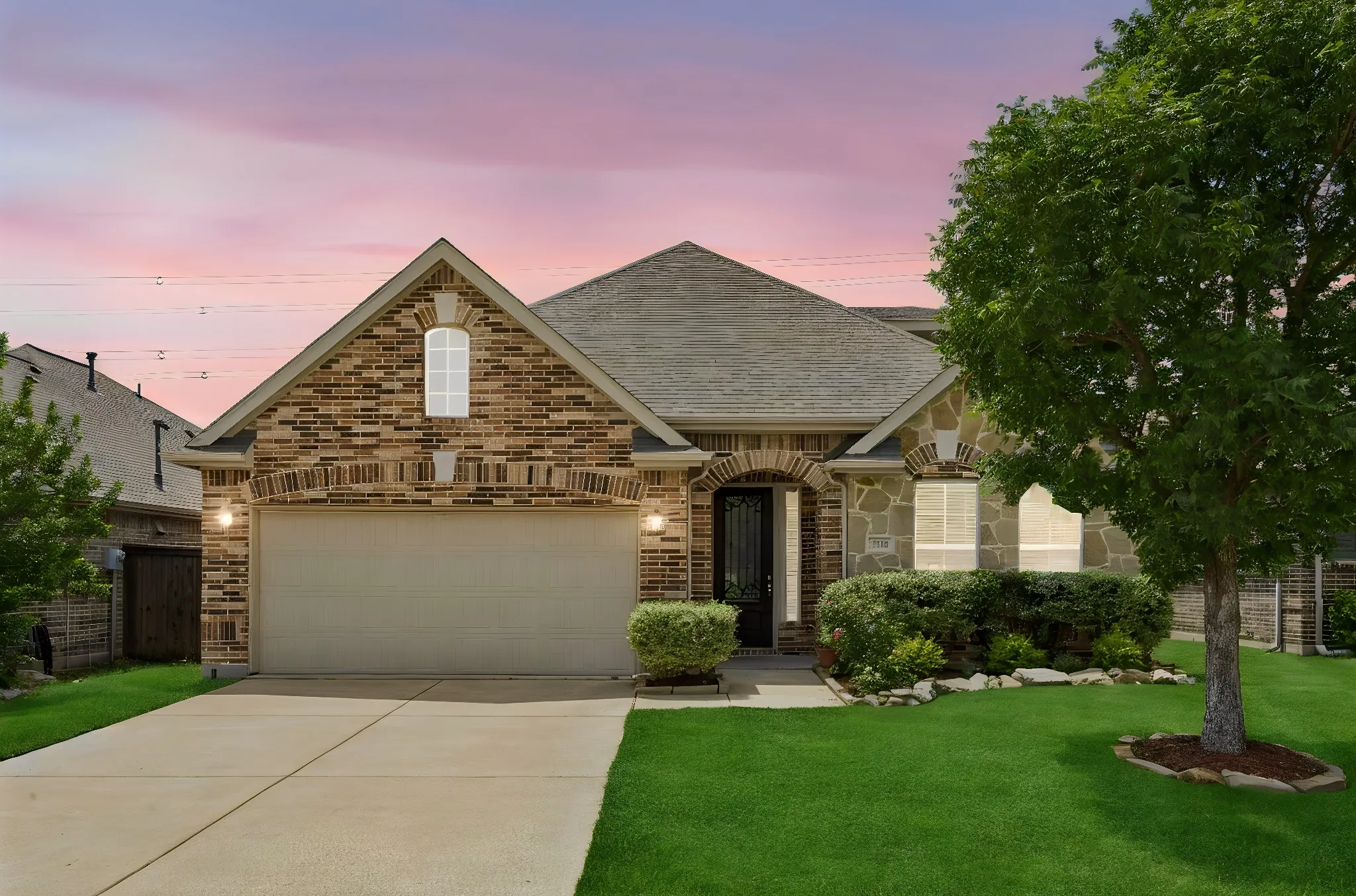 Brick and stone facade residence featuring an arched entry, attached garage, and manicured landscaping