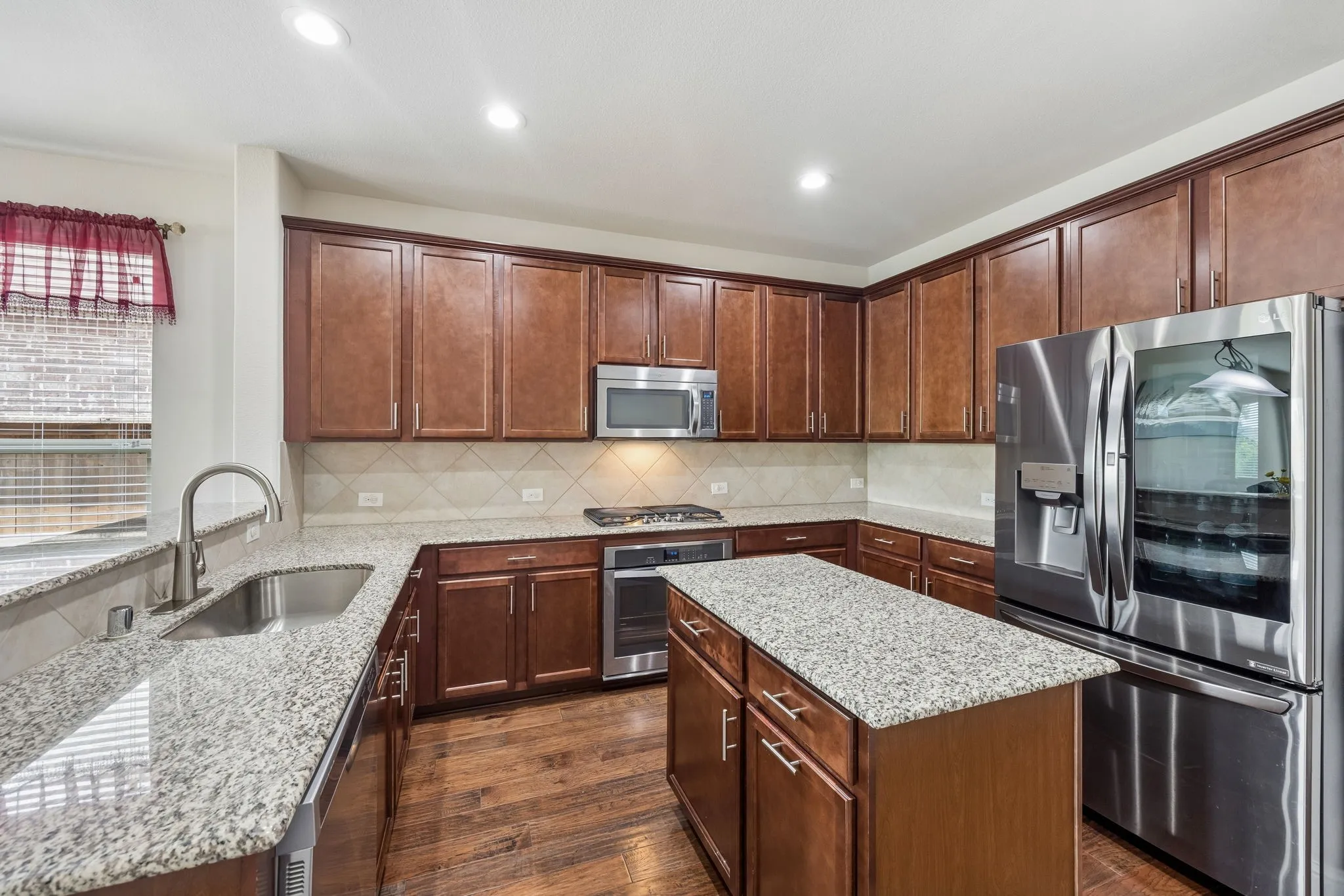Kitchen featuring wood flooring, granite countertops, wood cabinetry, stainless steel appliances, and an island with additional counter space