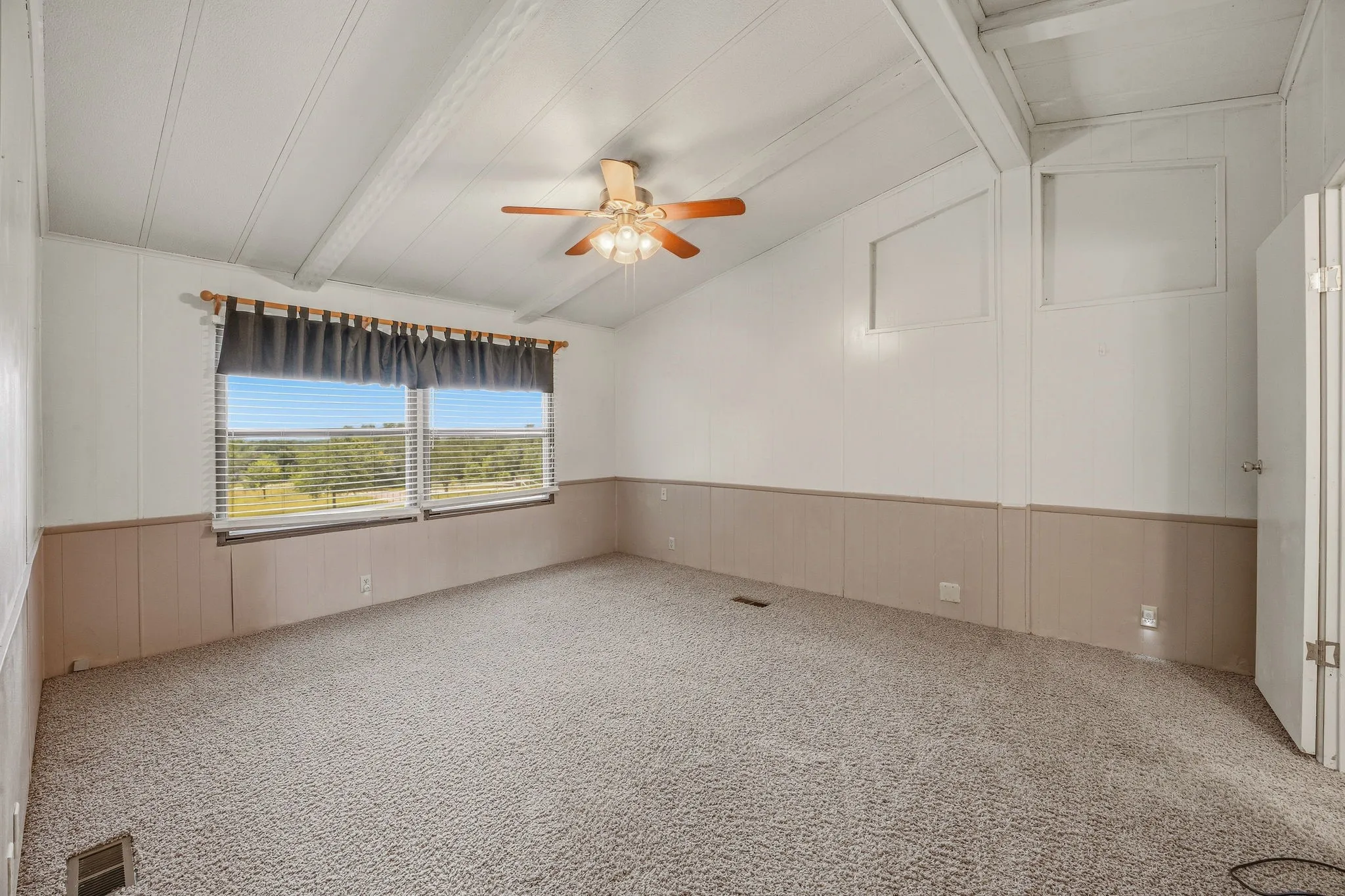 Room featuring vaulted ceilings with exposed beams, two windows with blinds, a ceiling fan with integrated lighting, and carpet flooring