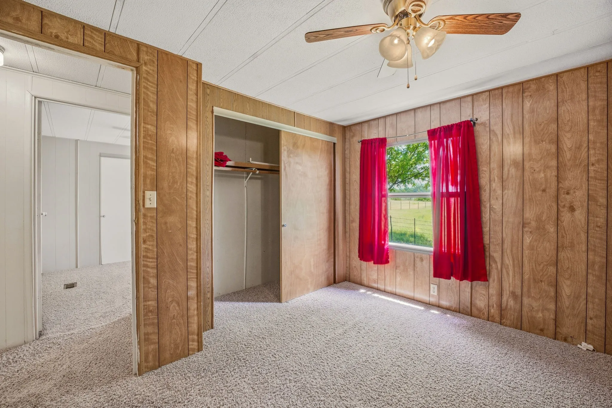 Carpeted interior space featuring wood-finish paneling walls and a window with a green outdoor scene