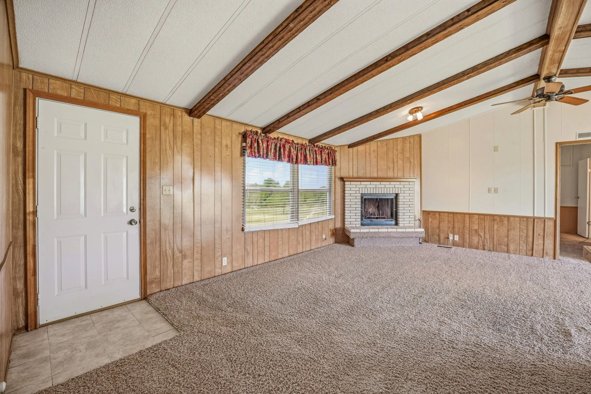 Living area featuring a brick fireplace, vaulted ceiling with exposed wood beams, and a ceiling fan