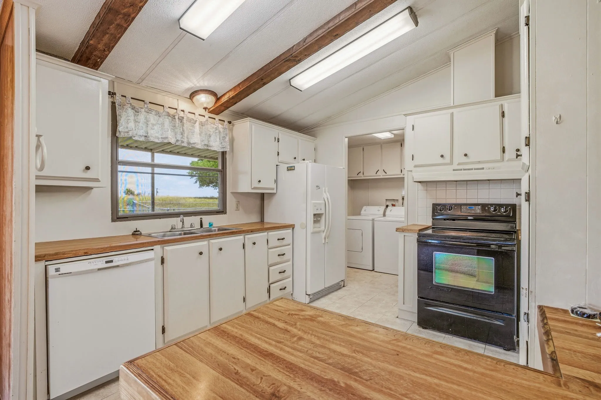 Kitchen featuring white cabinetry, wood-finish countertops, stainless steel sink, and a black electric range