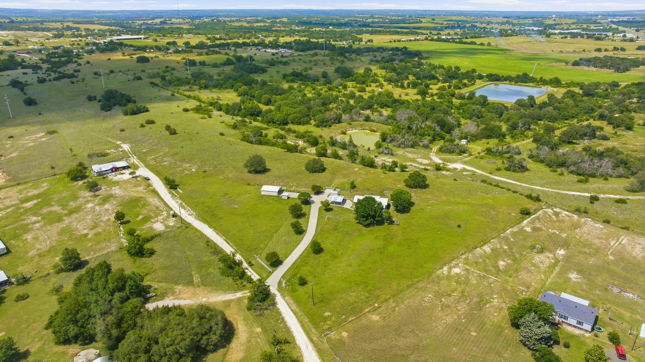 Expansive undeveloped land featuring multiple clearings, scattered mature trees, two visible ponds, and a winding unpaved road