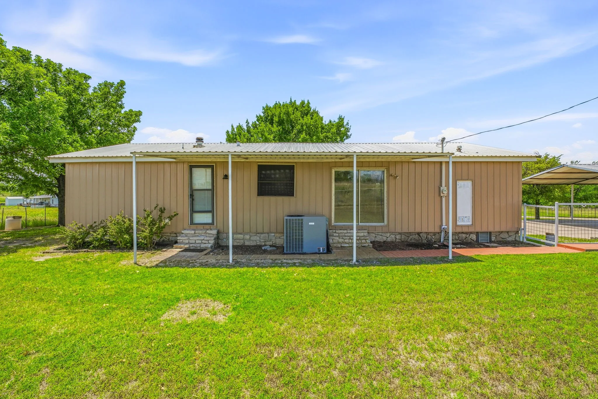 Rear exterior featuring a covered patio, tan vertical siding, a stone skirt, and a metal roof
