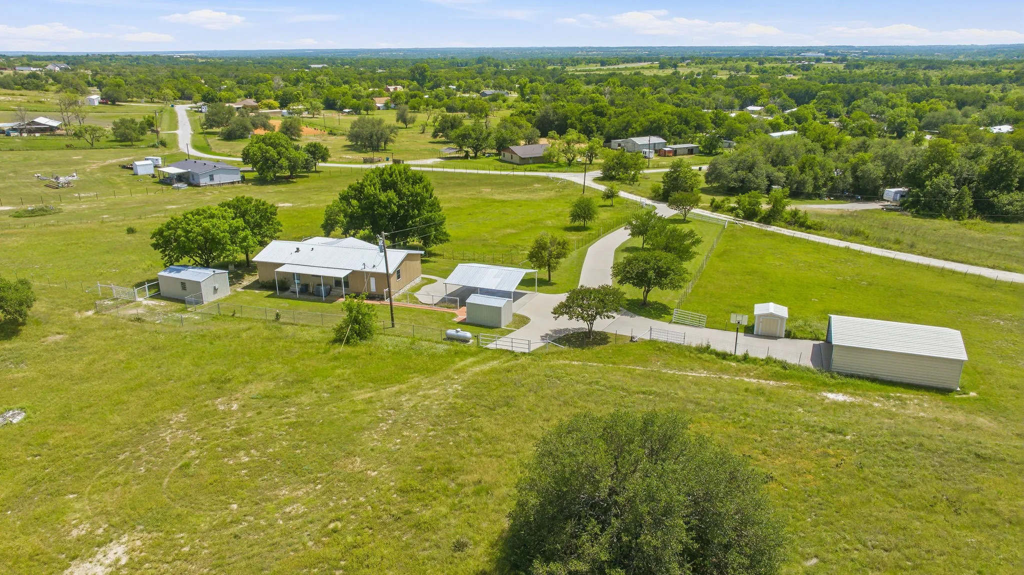 Single-story property with a light-colored exterior and covered front porch, set on a expansive green landscape