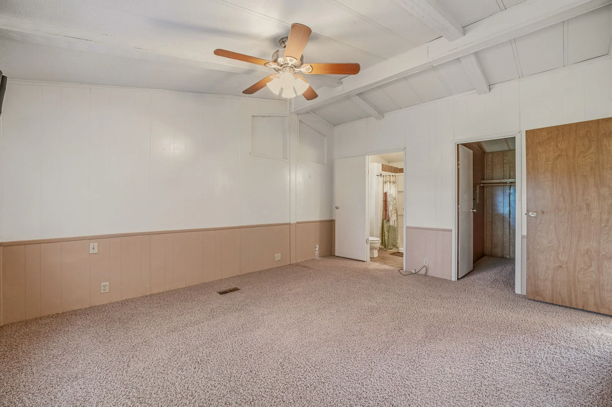 Carpeted room featuring a ceiling fan with light fixture, exposed beam ceiling, and paneled walls