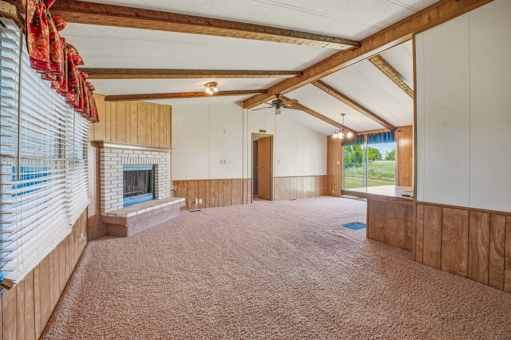 Living area featuring a brick fireplace with hearth, wood-finish accent paneling, and vaulted ceilings with exposed beams