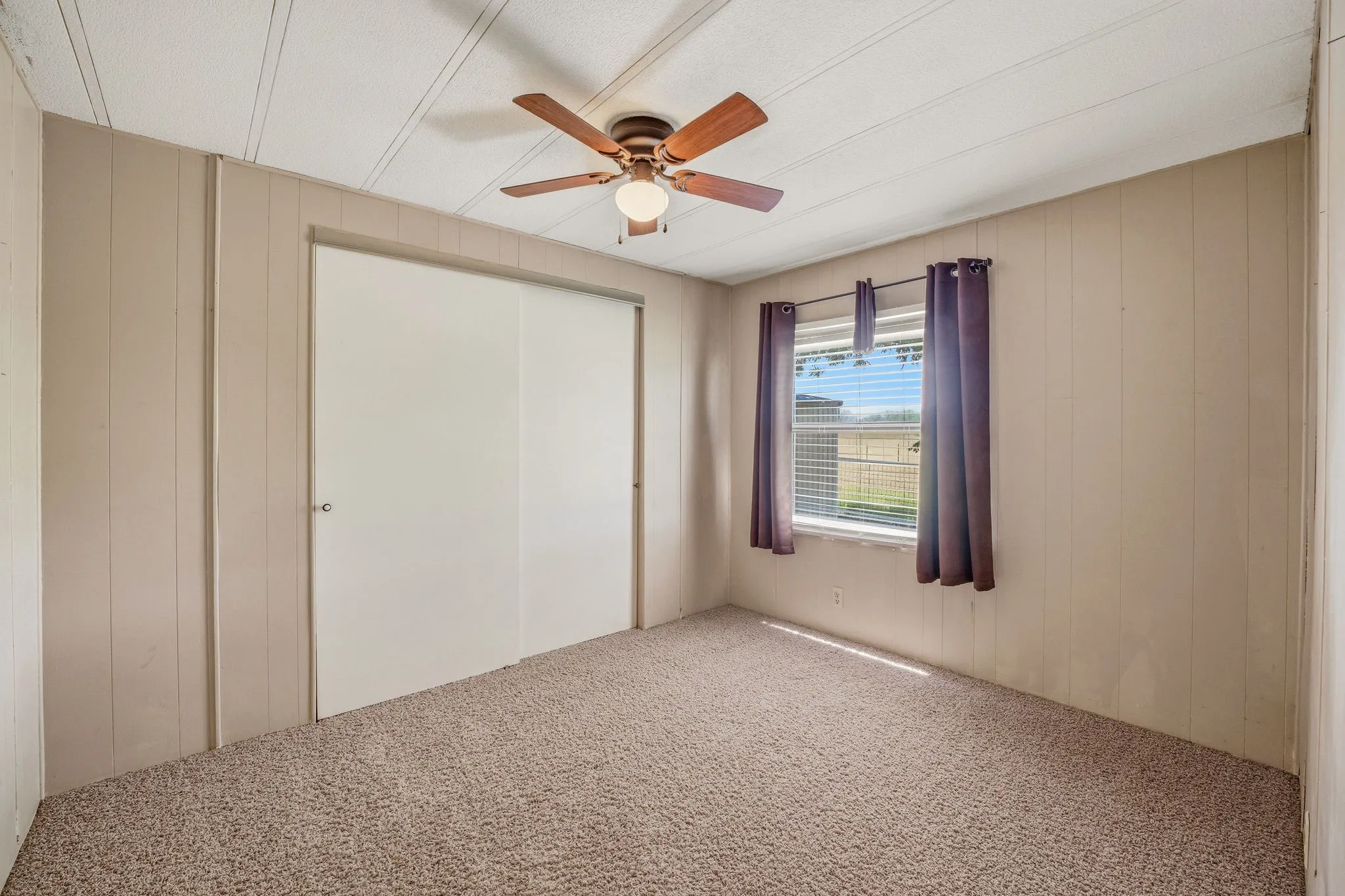 Carpeted room featuring a ceiling fan with integrated lighting, a window with horizontal blinds, and a built-in closet with sliding doors
